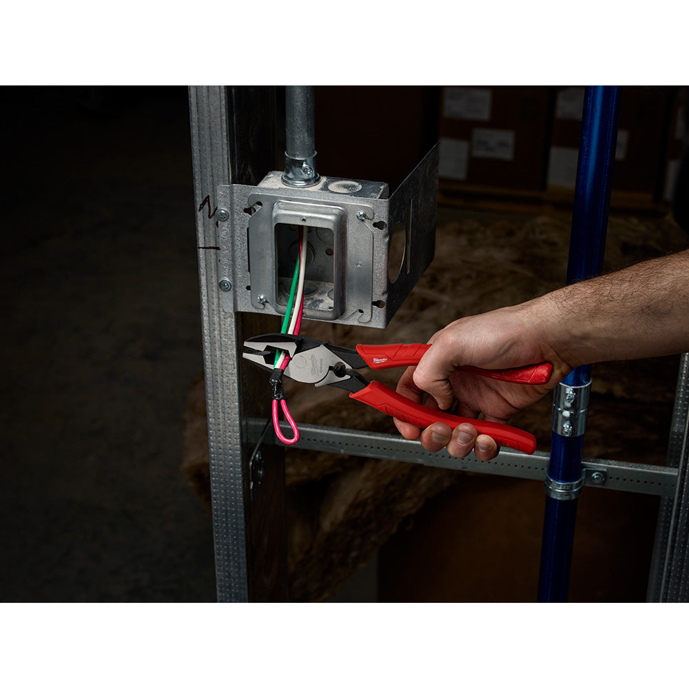 Red lineman's pliers with crimper being held near electrical wiring and junction box.