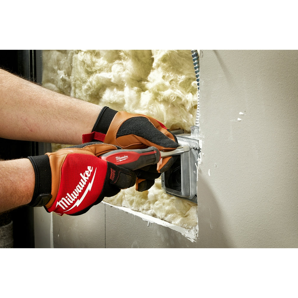 Tan leather gloves with red and black panels worn while installing insulation in a wall cavity.