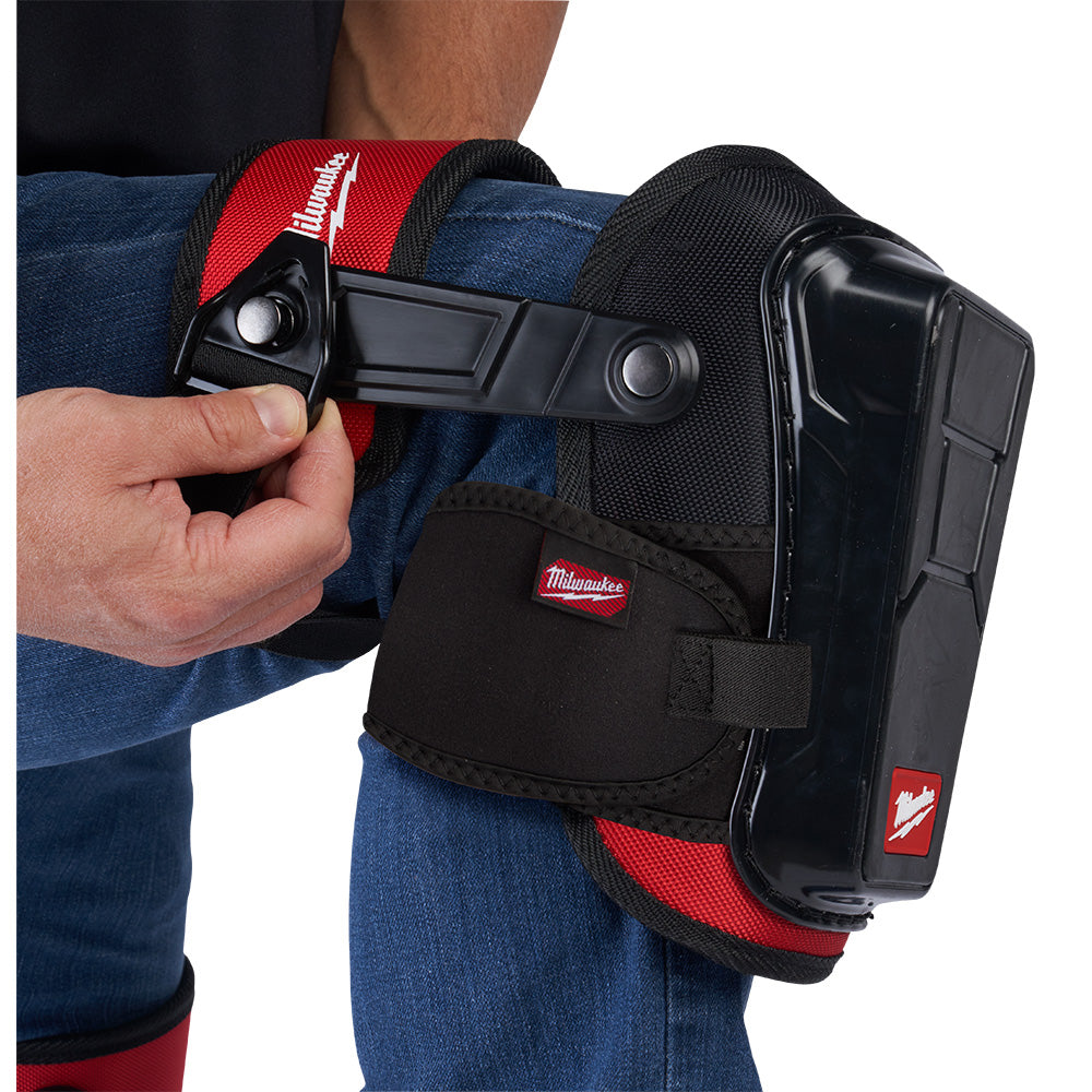 Black and red knee pads with hard shell protection and adjustable straps worn on legs, shown with fastening detail.