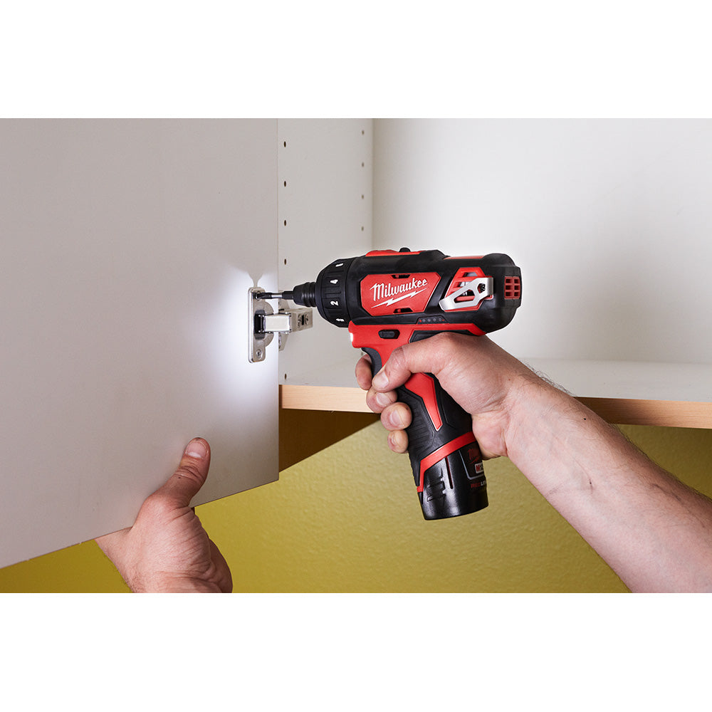 Red and black Milwaukee cordless screwdriver being held by a hand, driving a screw into drywall.