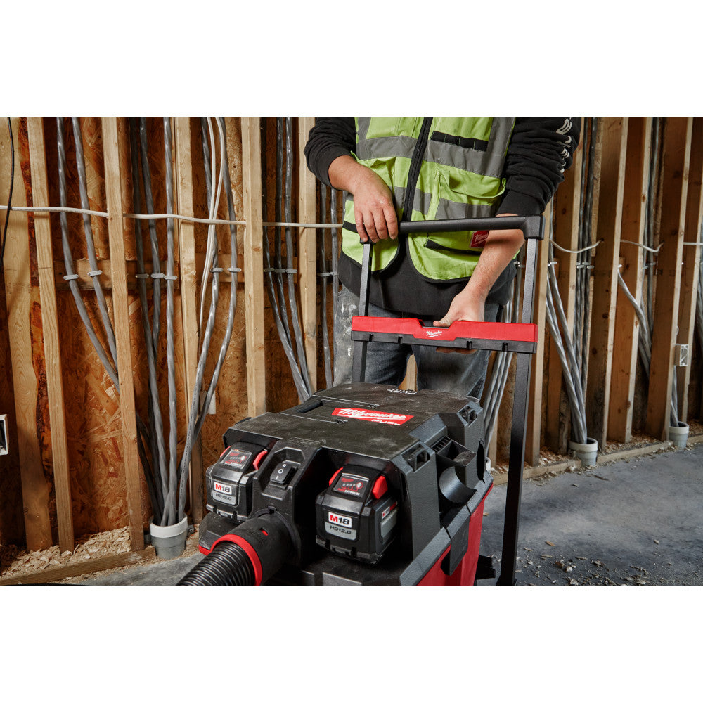 Milwaukee wet/dry vacuum cart with red frame, black tank, handle, and battery slots, being used on a job site.