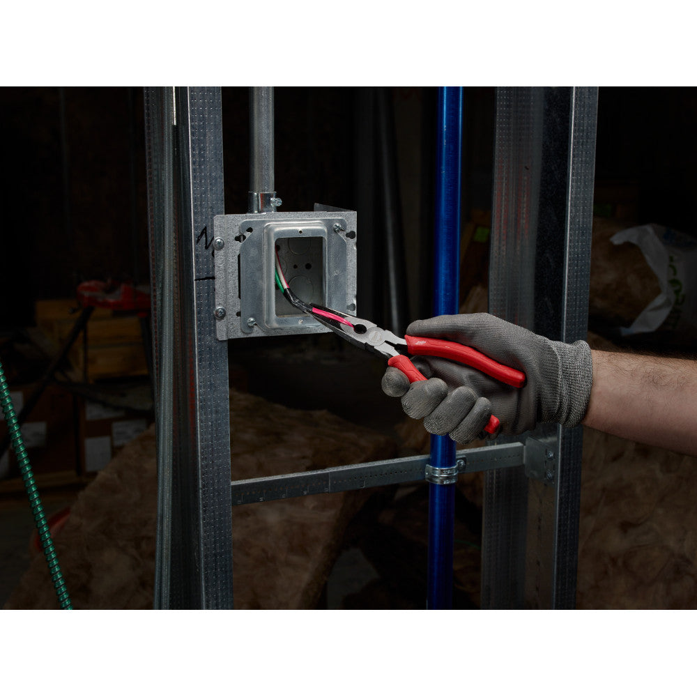 Red and gray long nose pliers held in a gloved hand while working on electrical wiring inside a wall outlet.