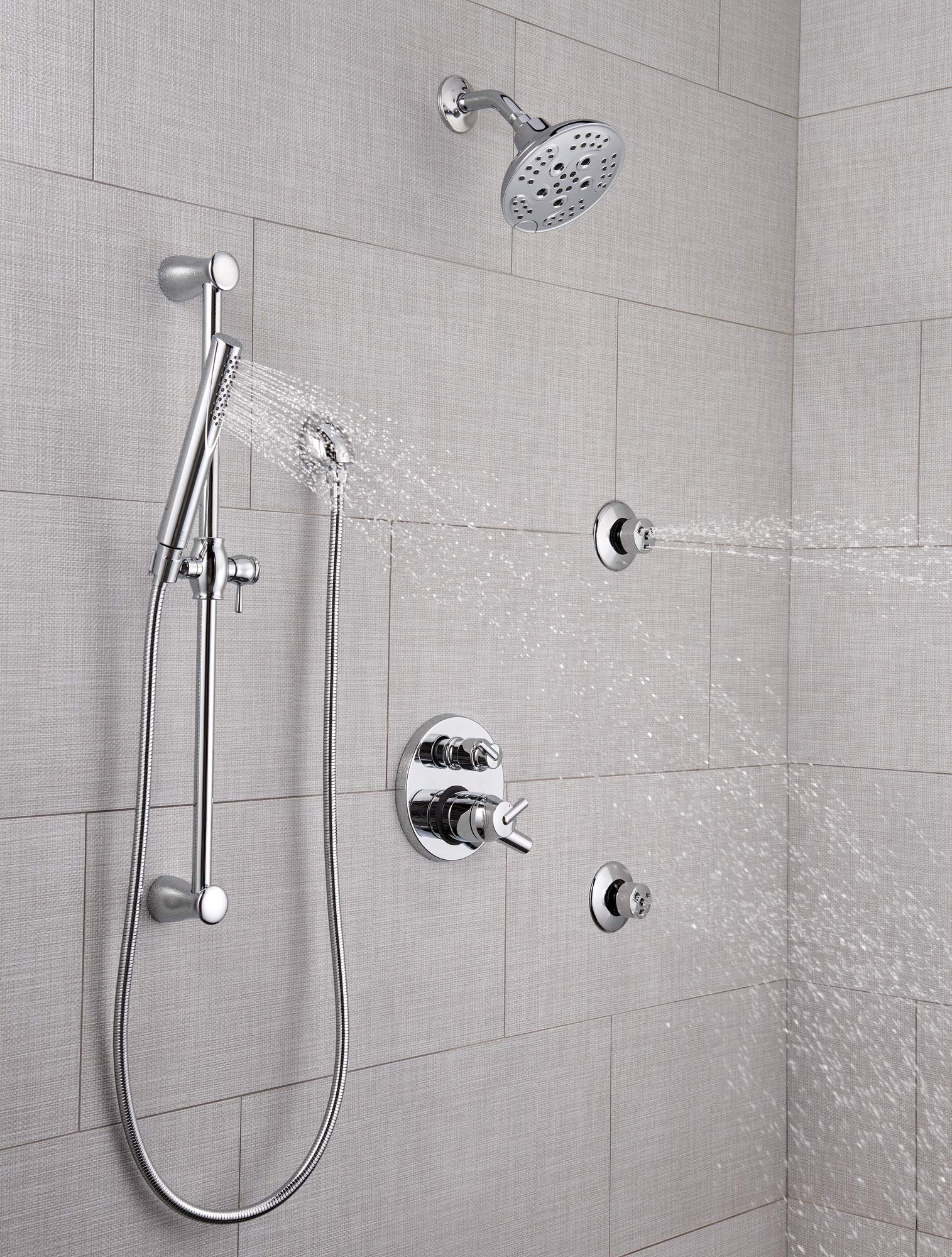 Chrome shower system with overhead rainfall showerhead, handheld wand, and multiple body jets mounted on tile wall.