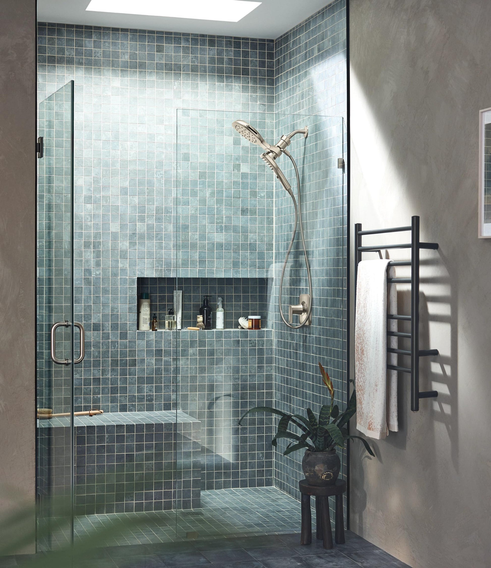Brushed nickel shower head with detachable hand shower mounted in modern tiled shower enclosure.