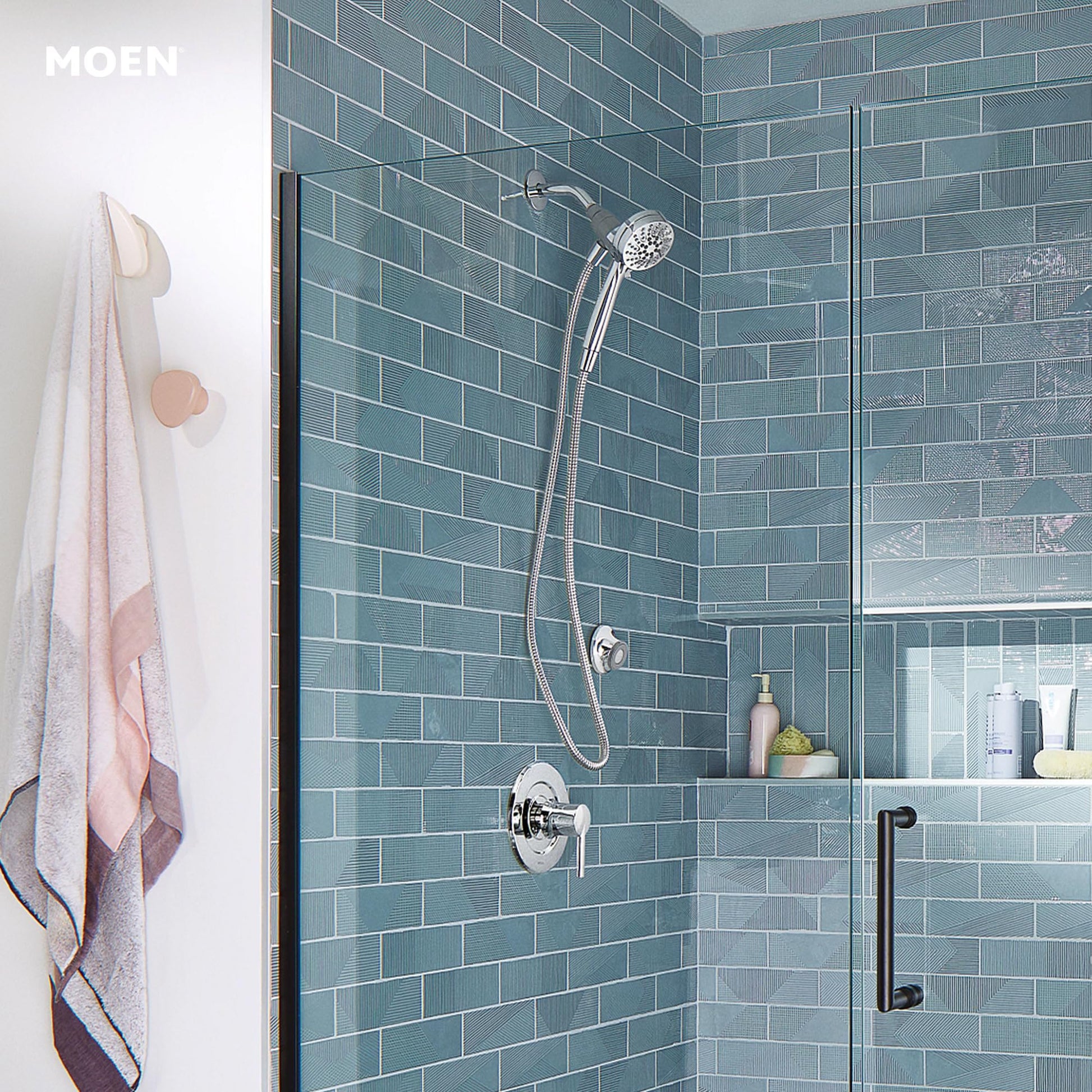 Chrome hand shower with flexible hose mounted on teal subway tile shower wall with control valve below.