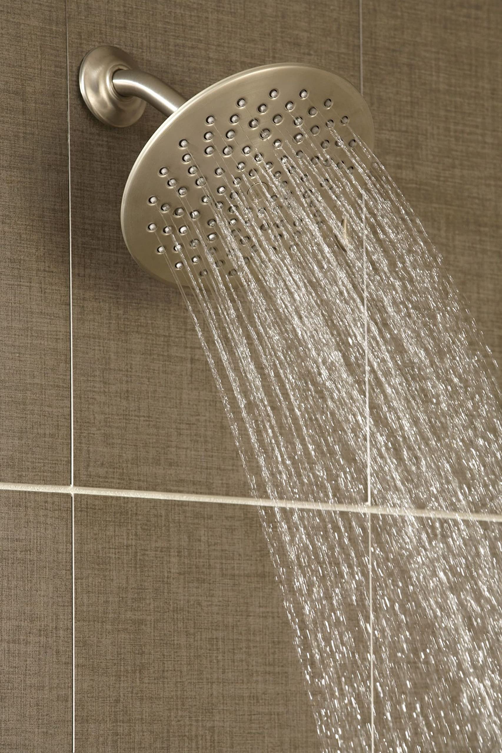 Brushed nickel 8-inch round rain shower head mounted on wall with curved arm, multiple spray jets visible with water flowing 