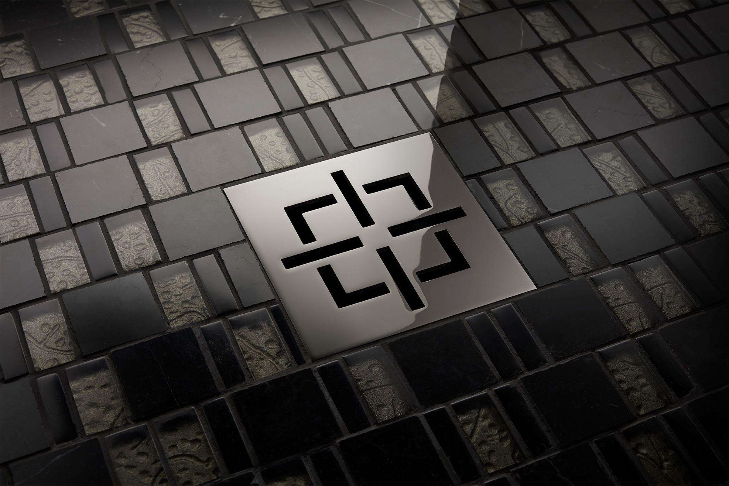 Satin brass square drain trim grid with geometric line pattern installed in tiled shower floor.