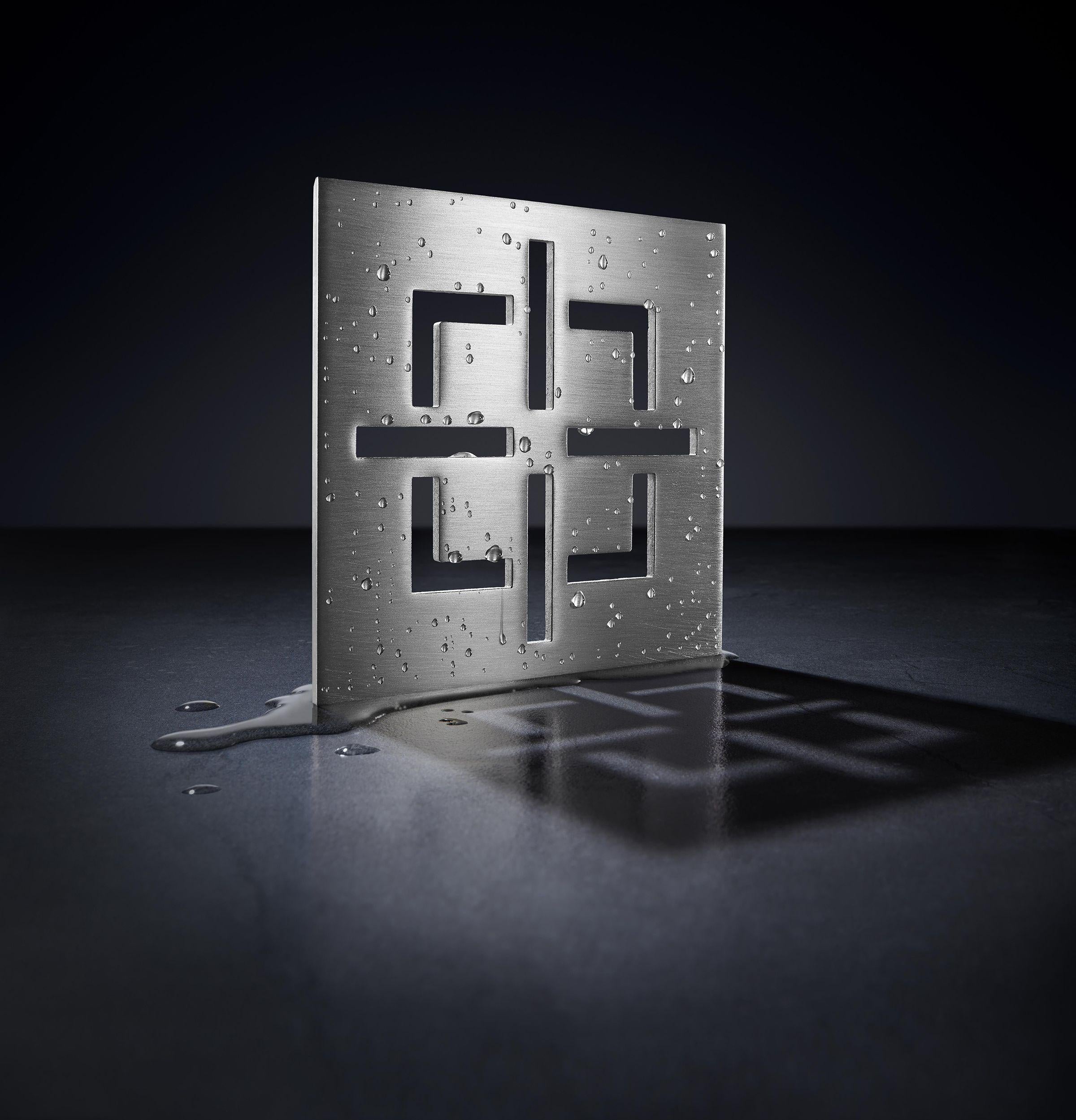 Satin brass drain trim grid with rectangular cutouts and mounting holes on perforated metal backing plate.