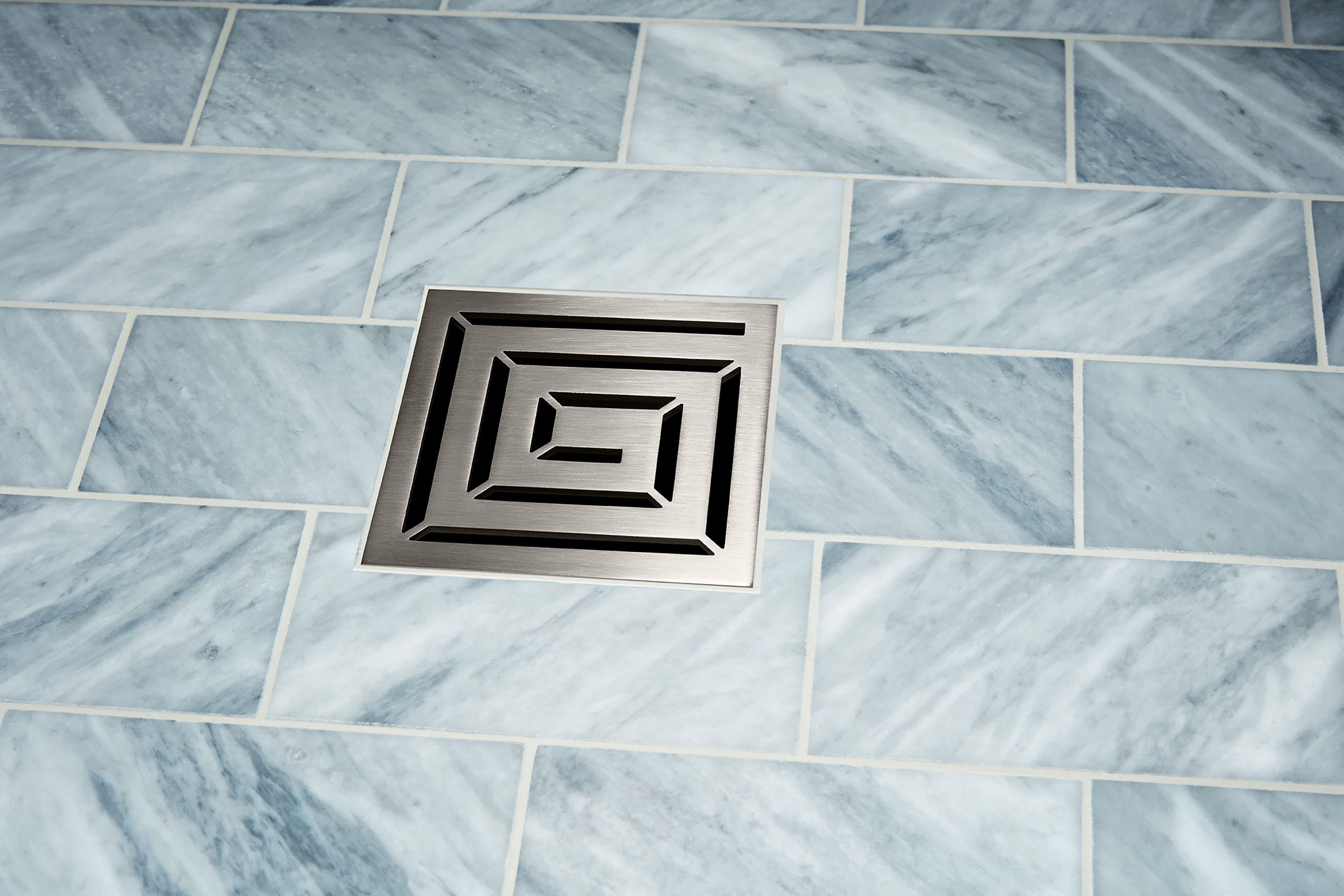 Satin nickel square drain trim with concentric rectangular grid pattern installed on marble tile.