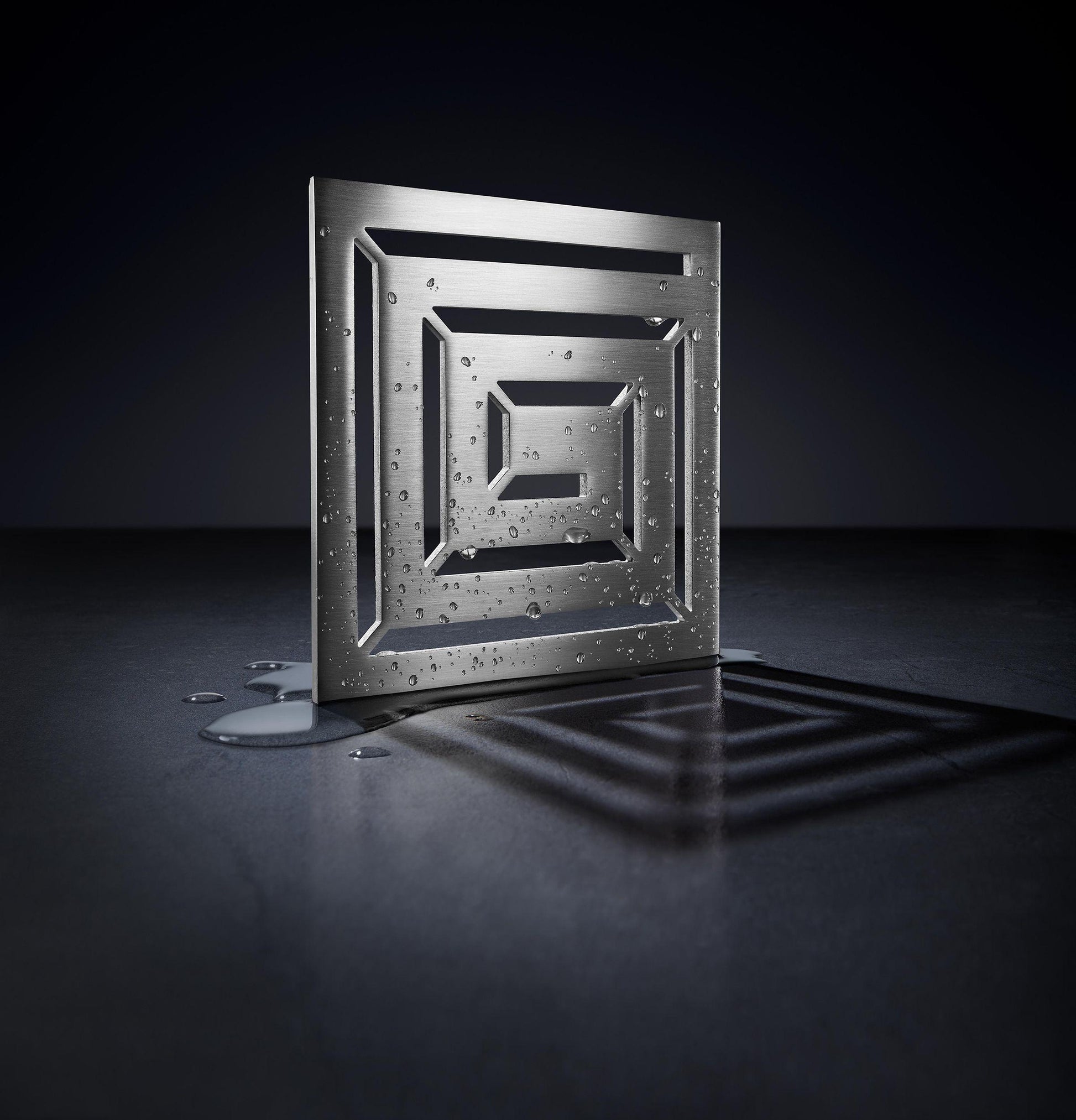 Satin nickel square drain trim with concentric grid pattern and water droplets on surface.