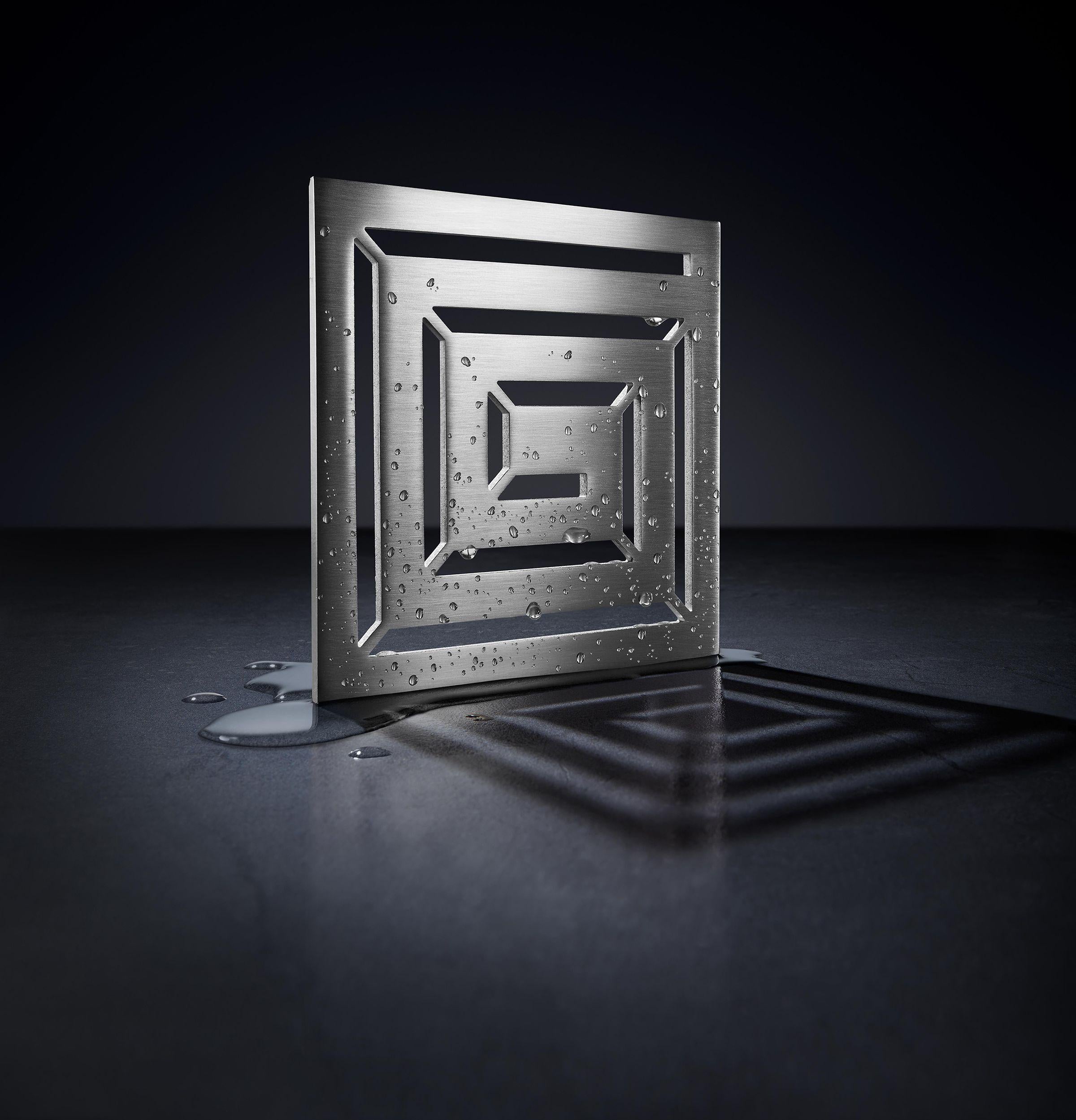 Satin nickel square drain trim with concentric grid pattern and water droplets on surface.