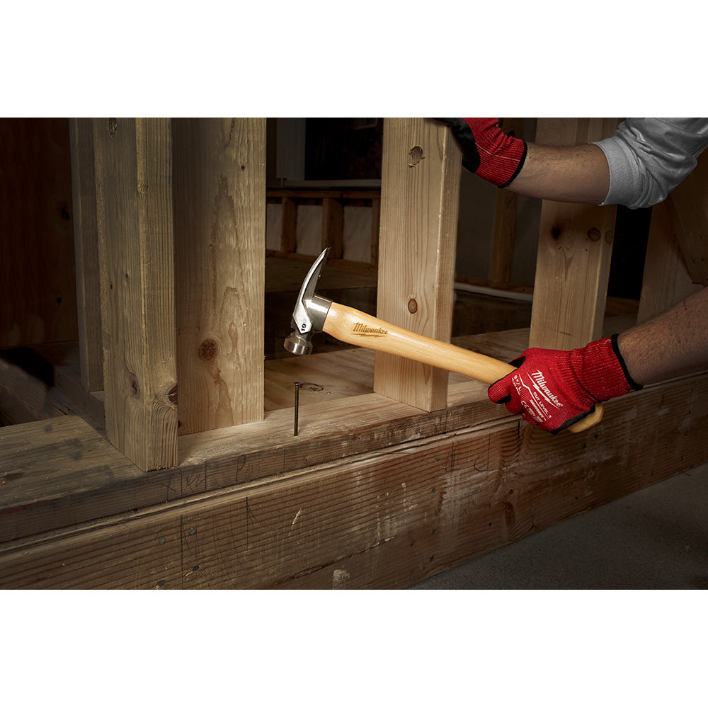 Milwaukee framing hammer with hickory wood handle and smooth metal head being used to drive a nail into lumber.