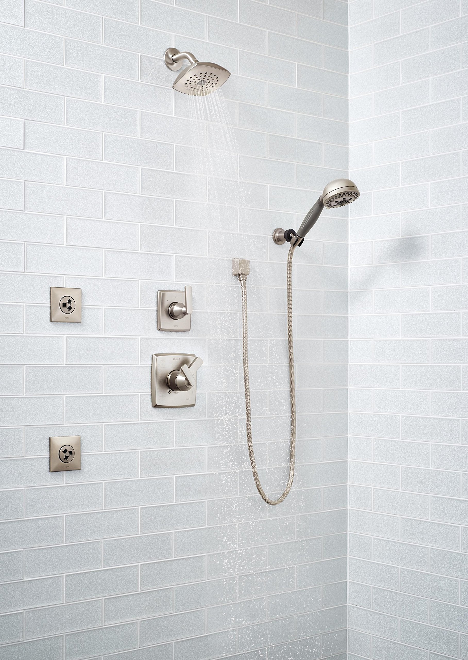Stainless steel square wall elbow mounted between shower head and hand shower on white subway tile wall.