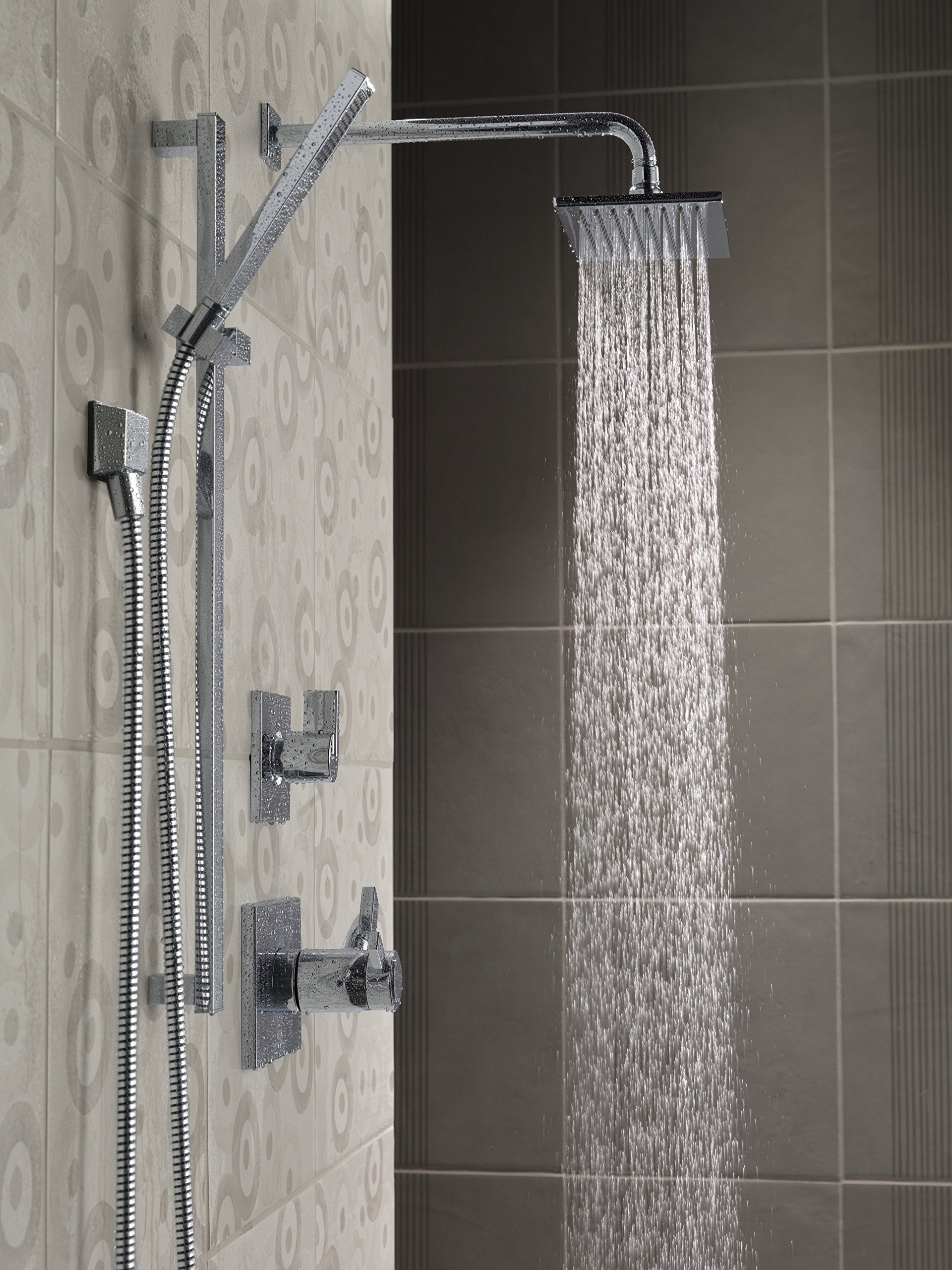 Chrome square wall elbow with hand shower and hose mounted on tiled bathroom wall.
