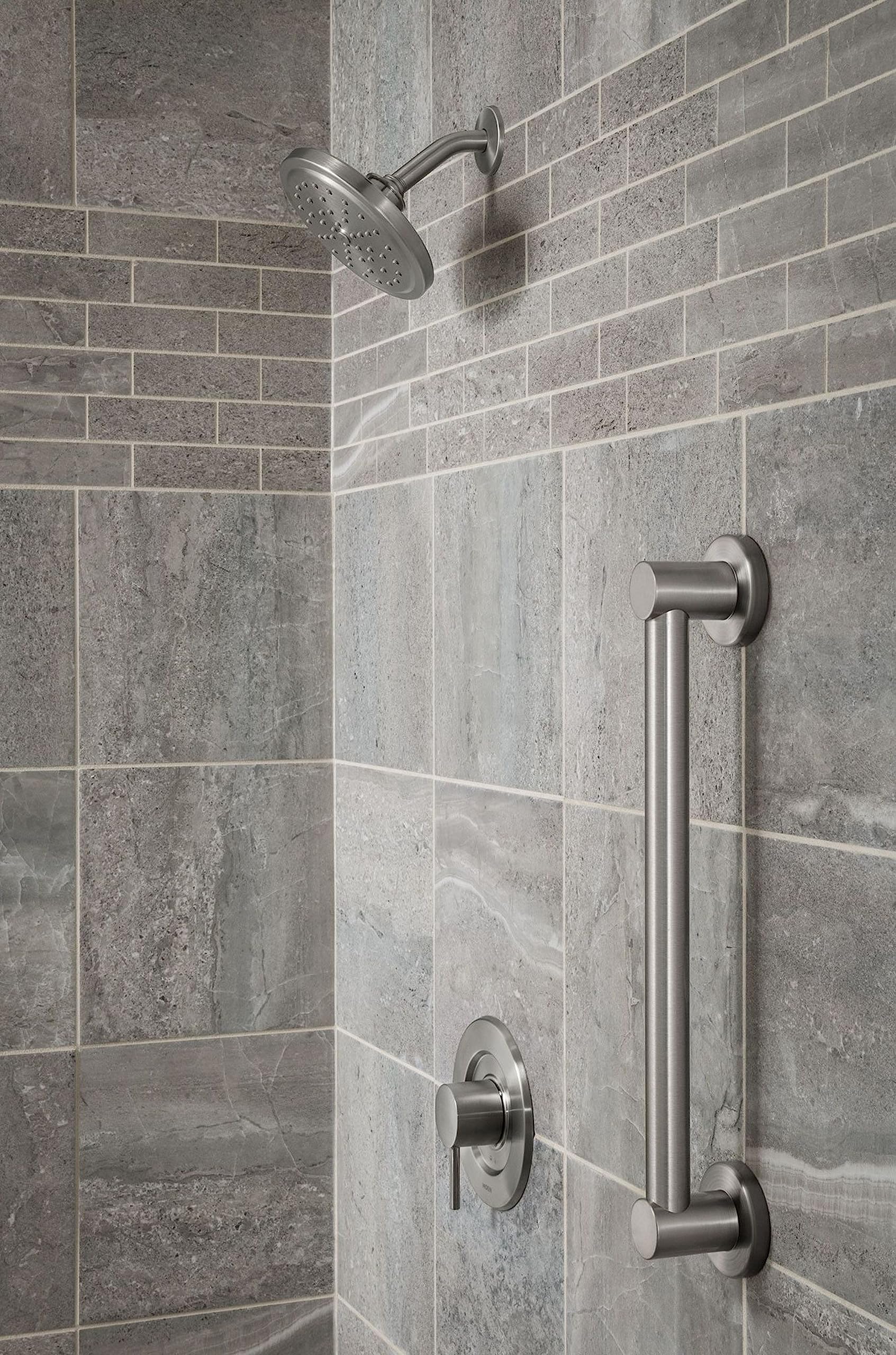 Brushed nickel stainless steel grab bar mounted vertically on tile bathroom wall next to showerhead.