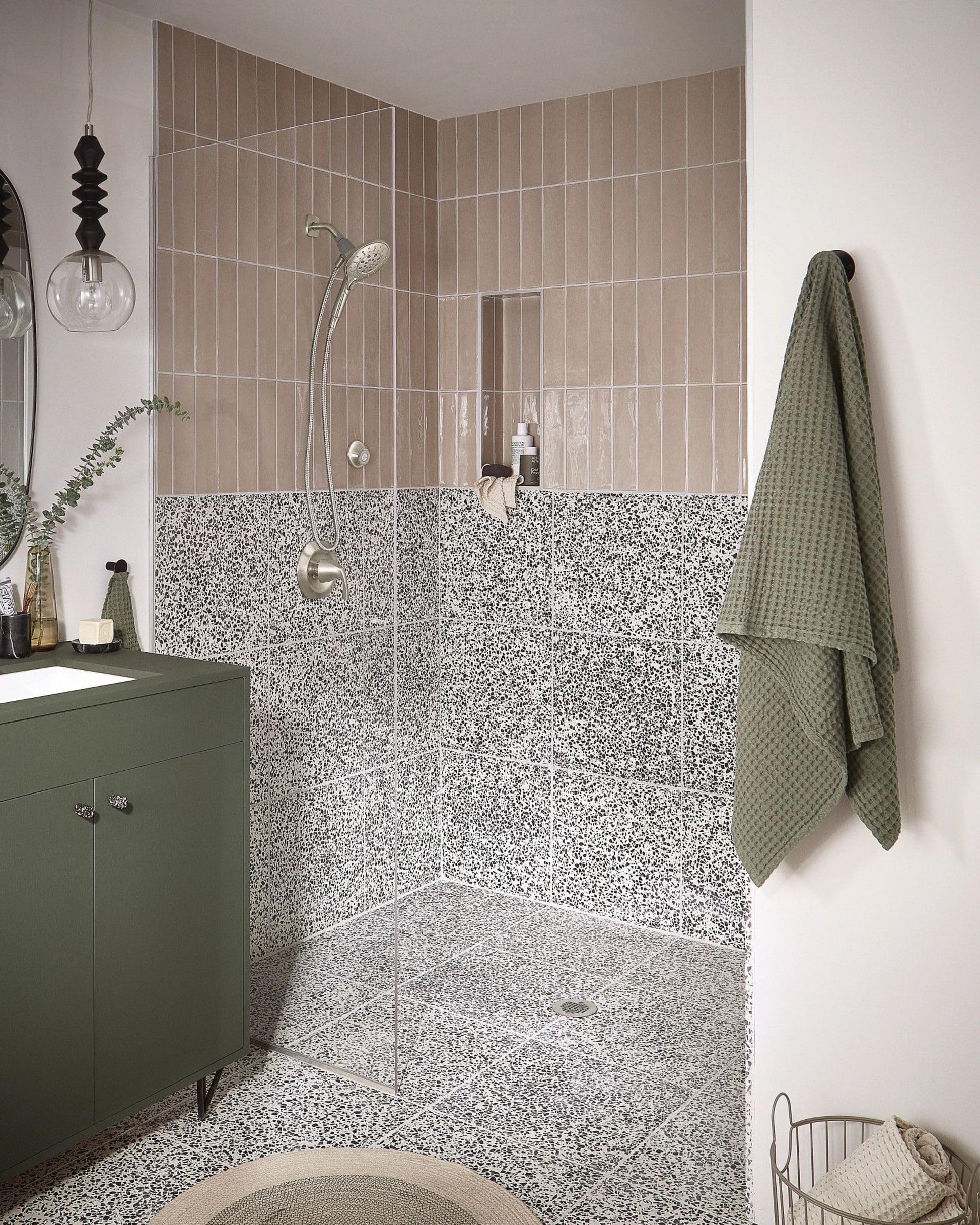 Brushed nickel showerhead with handheld attachment mounted on shower wall in bathroom with terrazzo tile surround.