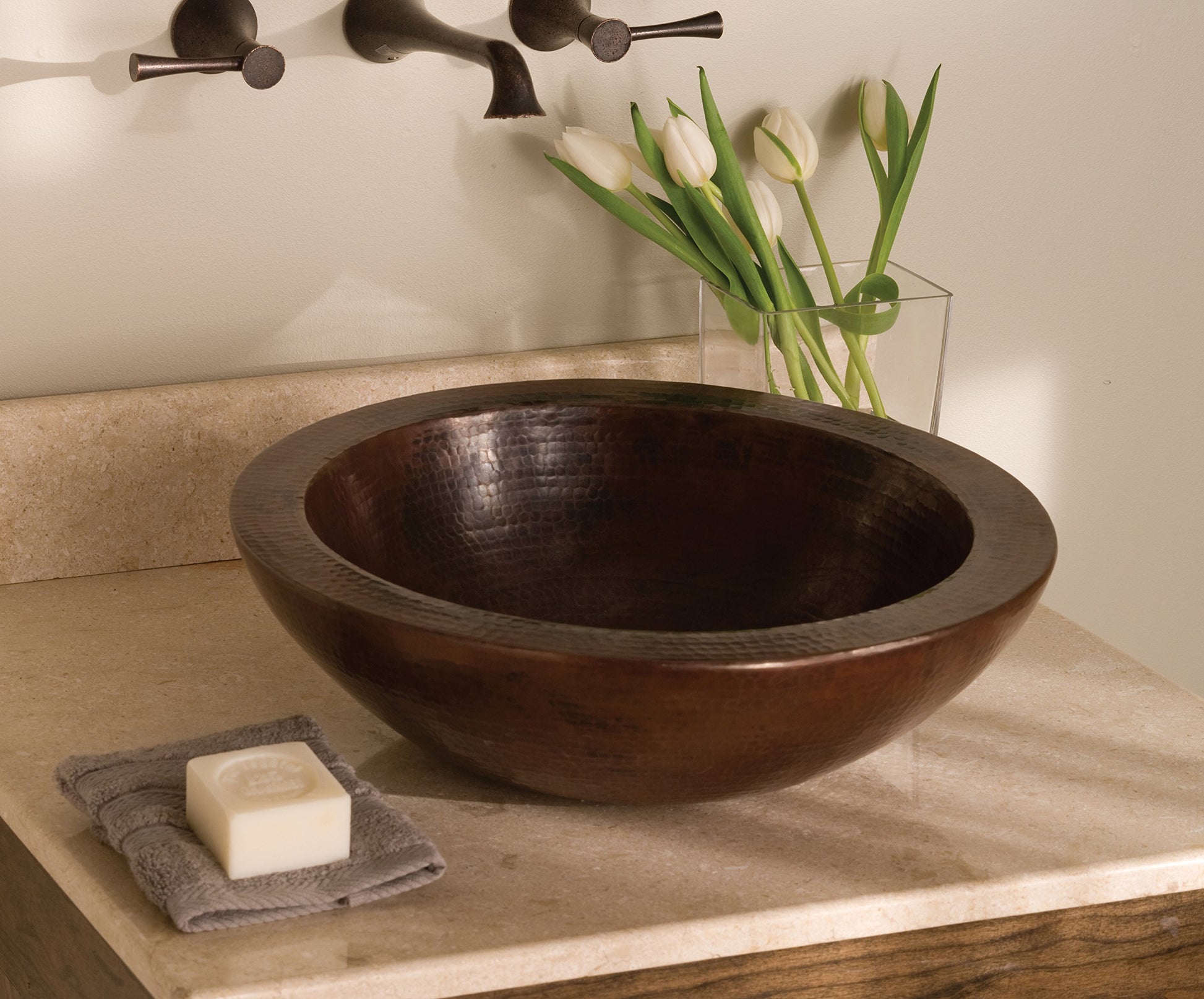Round hammered copper vessel sink with antique dark finish on stone countertop with faucet.