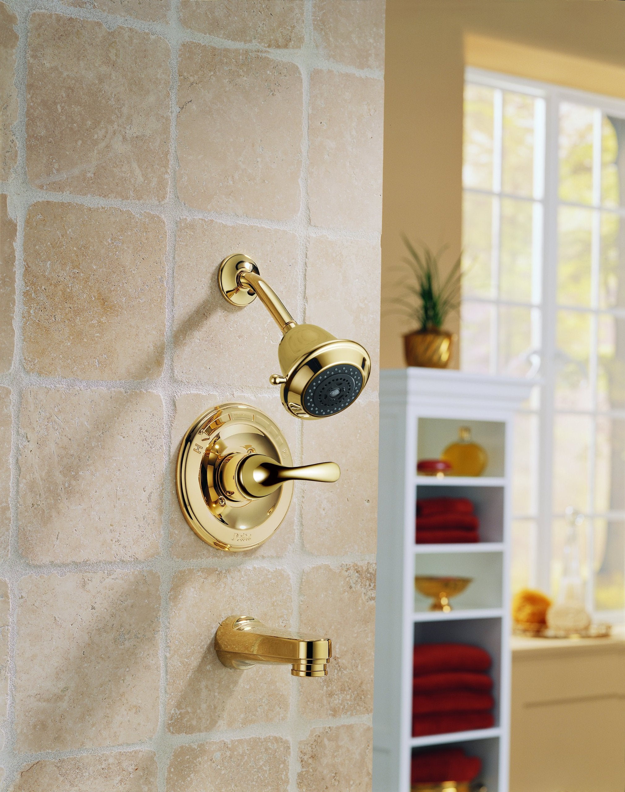 Polished brass tub and shower trim with single lever handle, showerhead, and tub spout mounted on stone tile wall.