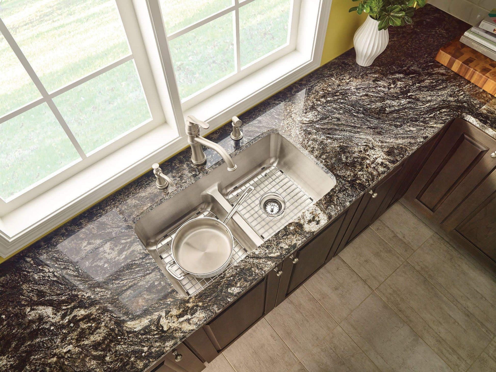 Stainless steel kitchen faucet with high arc spout and side spray mounted above double sink with granite countertop.