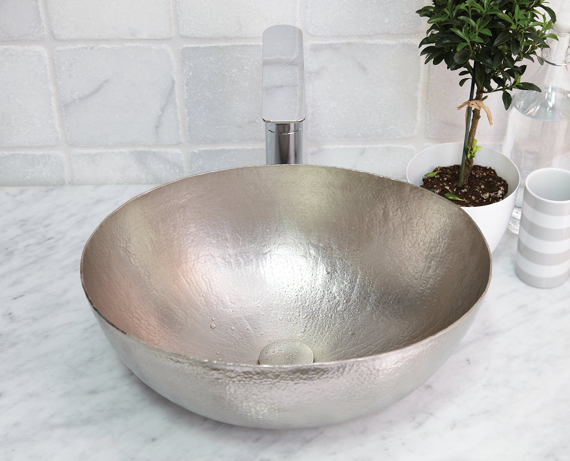 Hammered copper oval vessel sink with antique finish on marble countertop with chrome faucet.