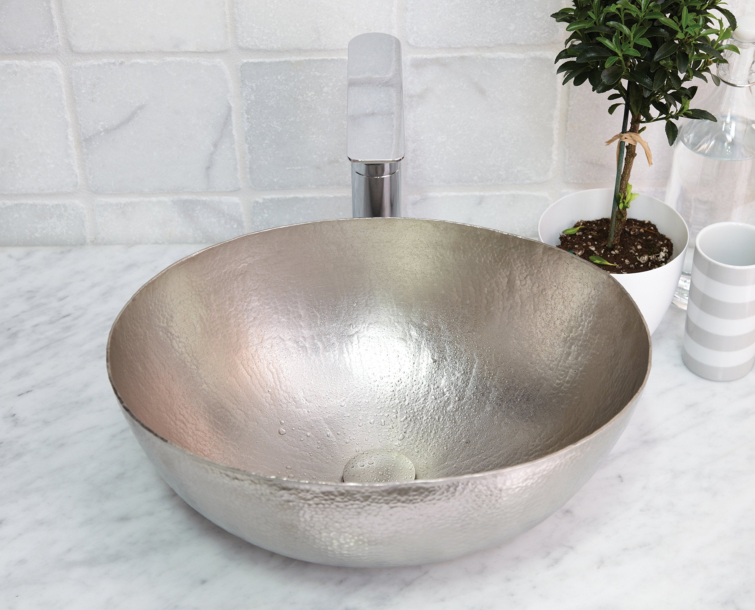 Hammered copper oval vessel sink with antique finish on marble countertop with chrome faucet.