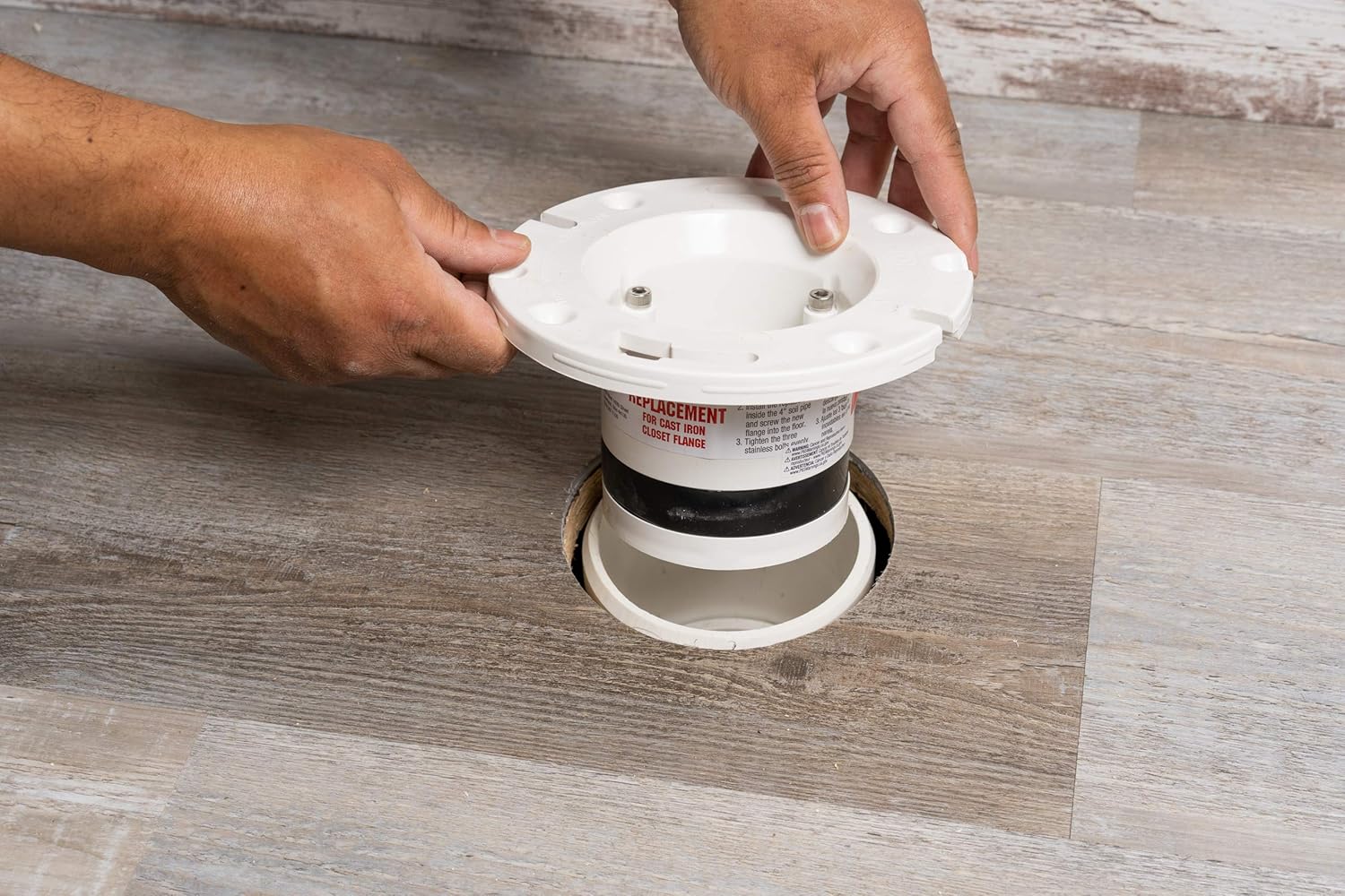 White PVC flange with rubber gasket and mounting bolts being held above floor opening.