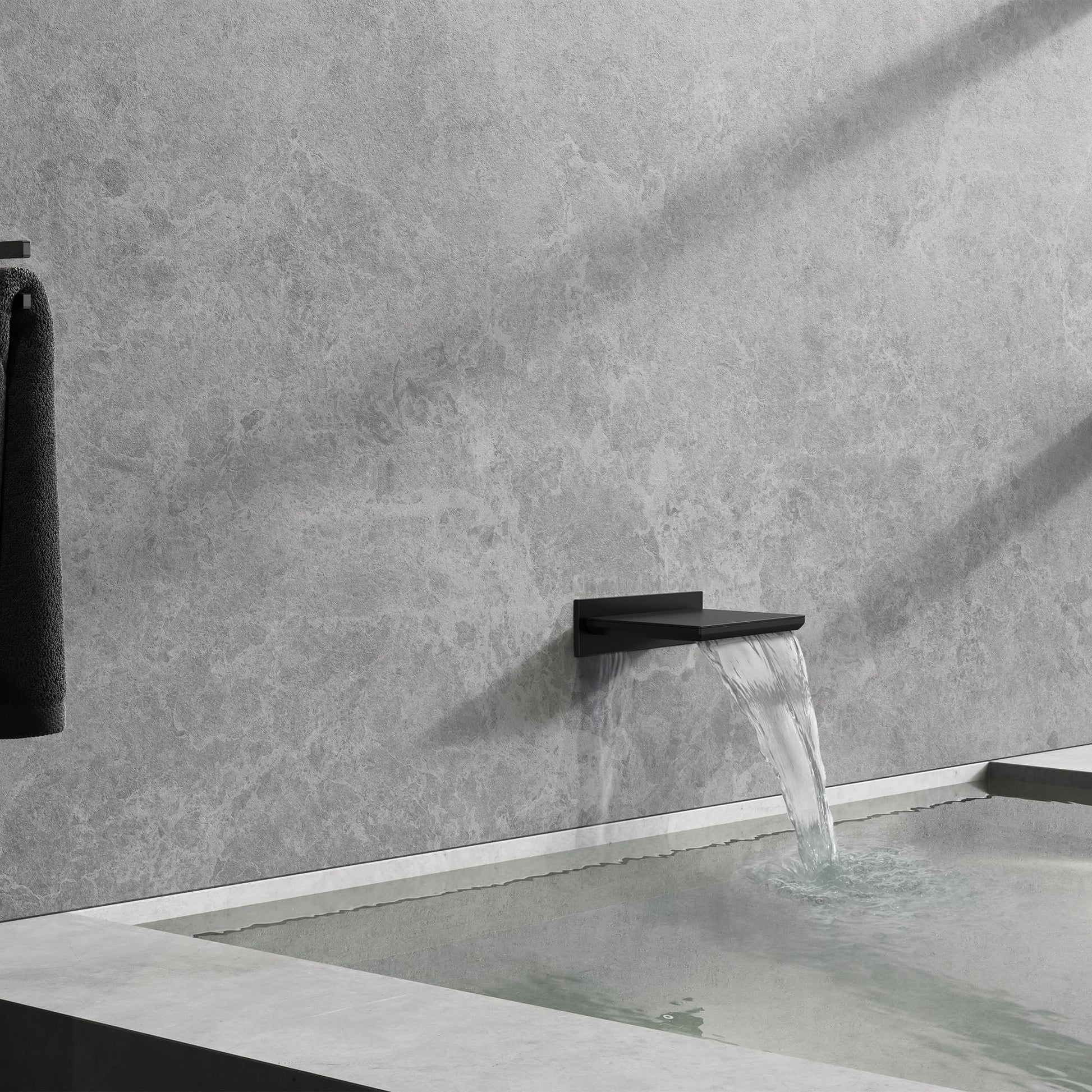 Black waterfall tub spout mounted on gray tile wall with water flowing into white bathtub.