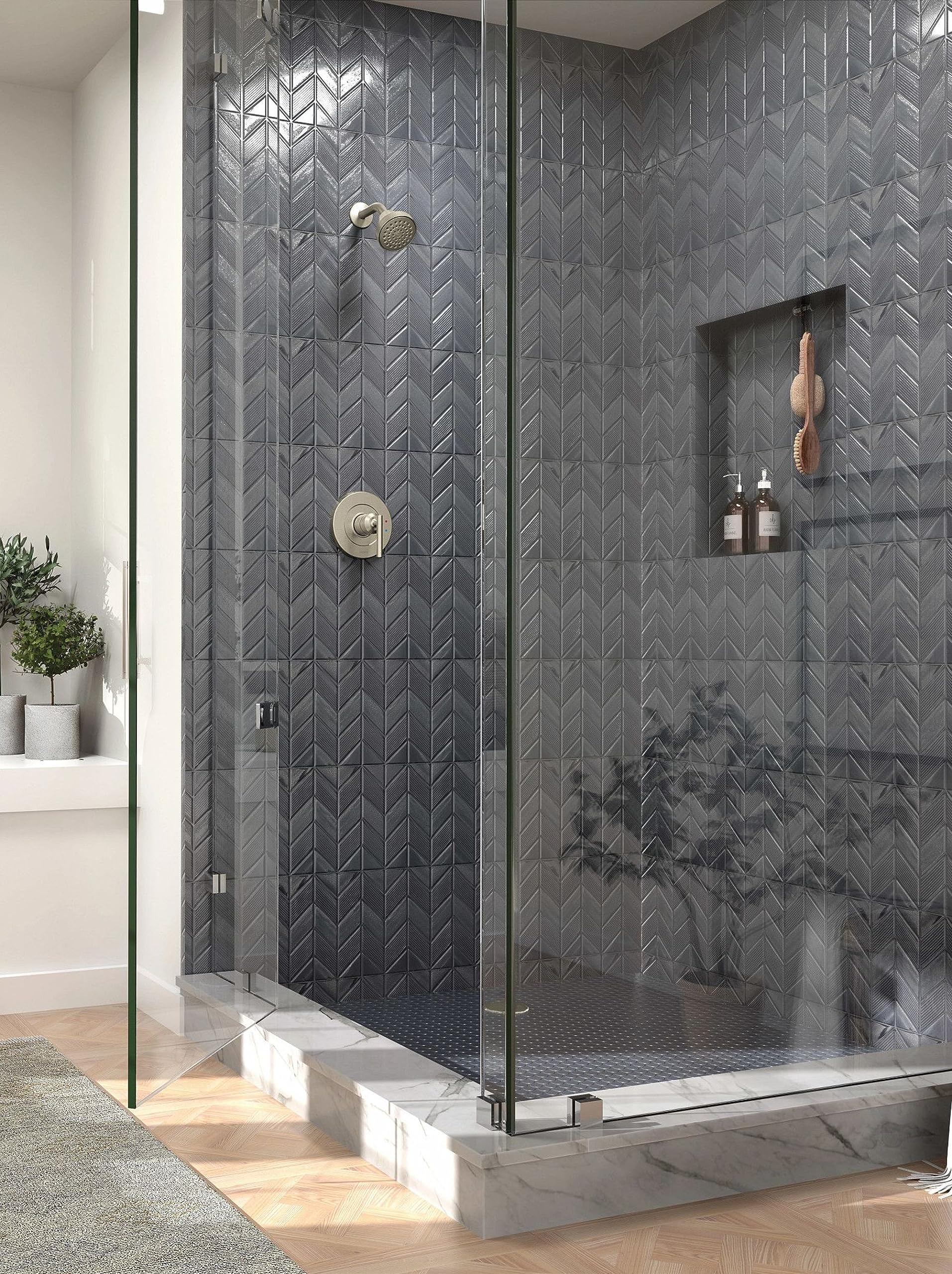 Brushed nickel single-handle shower trim with round trim plate and showerhead mounted on dark herringbone tile shower wall.