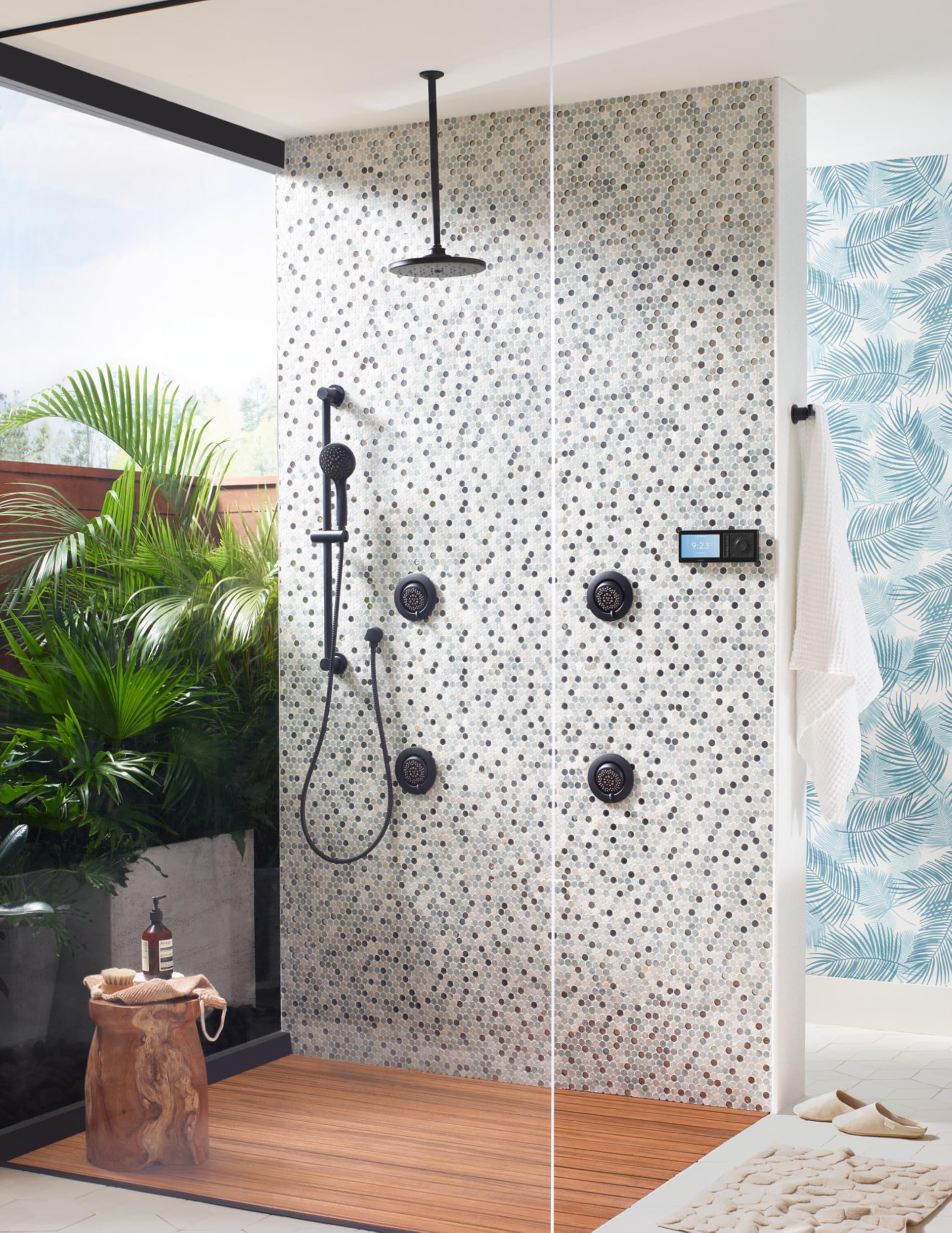 Matte black round shower spray system with ceiling mount, handheld wand, and four body jets installed on mosaic tile wall.