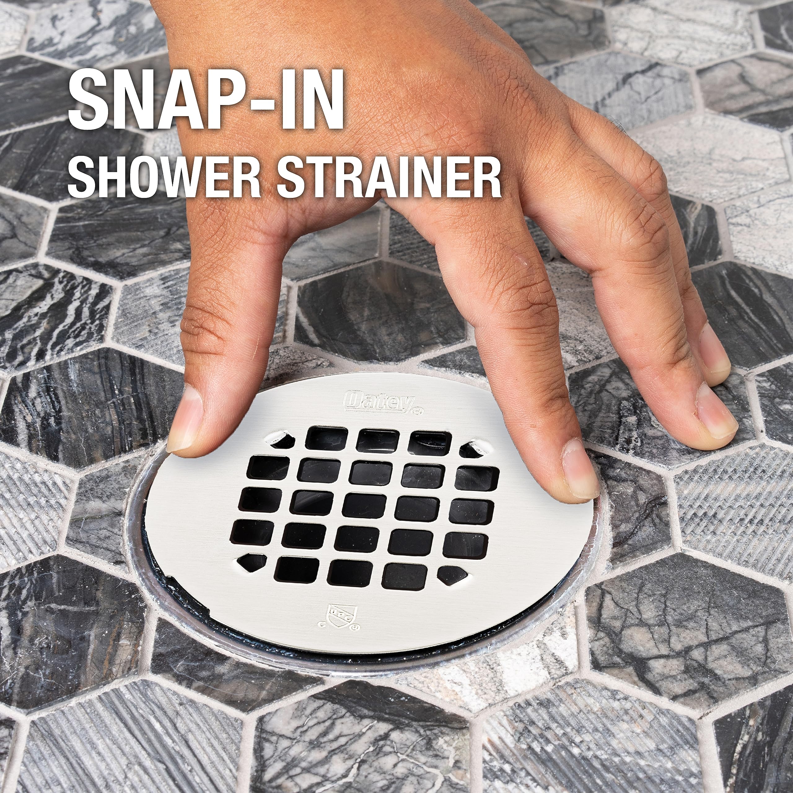 Satin nickel snap-in shower strainer with grid pattern holes, shown installed in tile floor with hand demonstrating snap mech