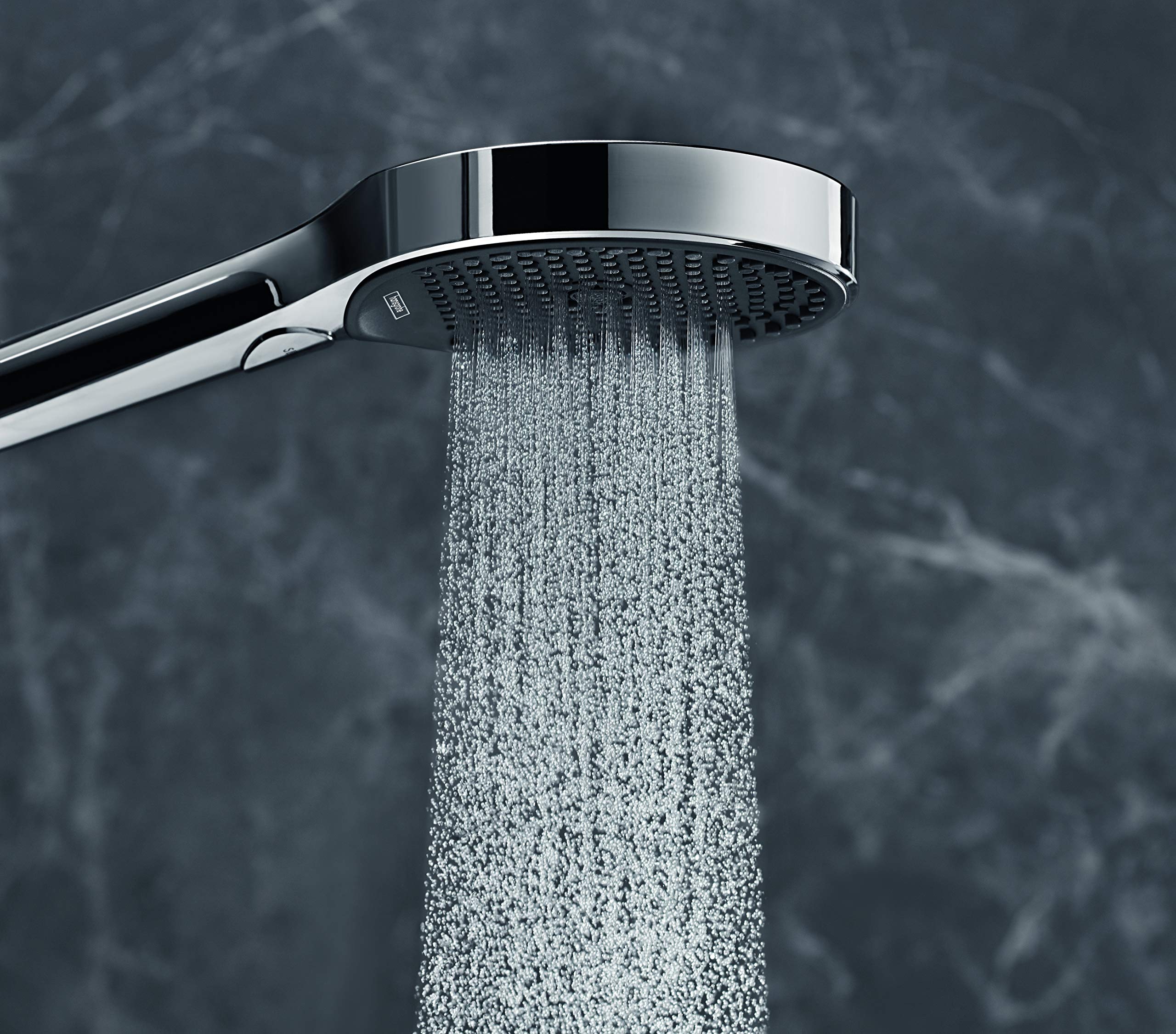 Chrome handheld showerhead with perforated face and hose, dispersing water spray against tiled background.