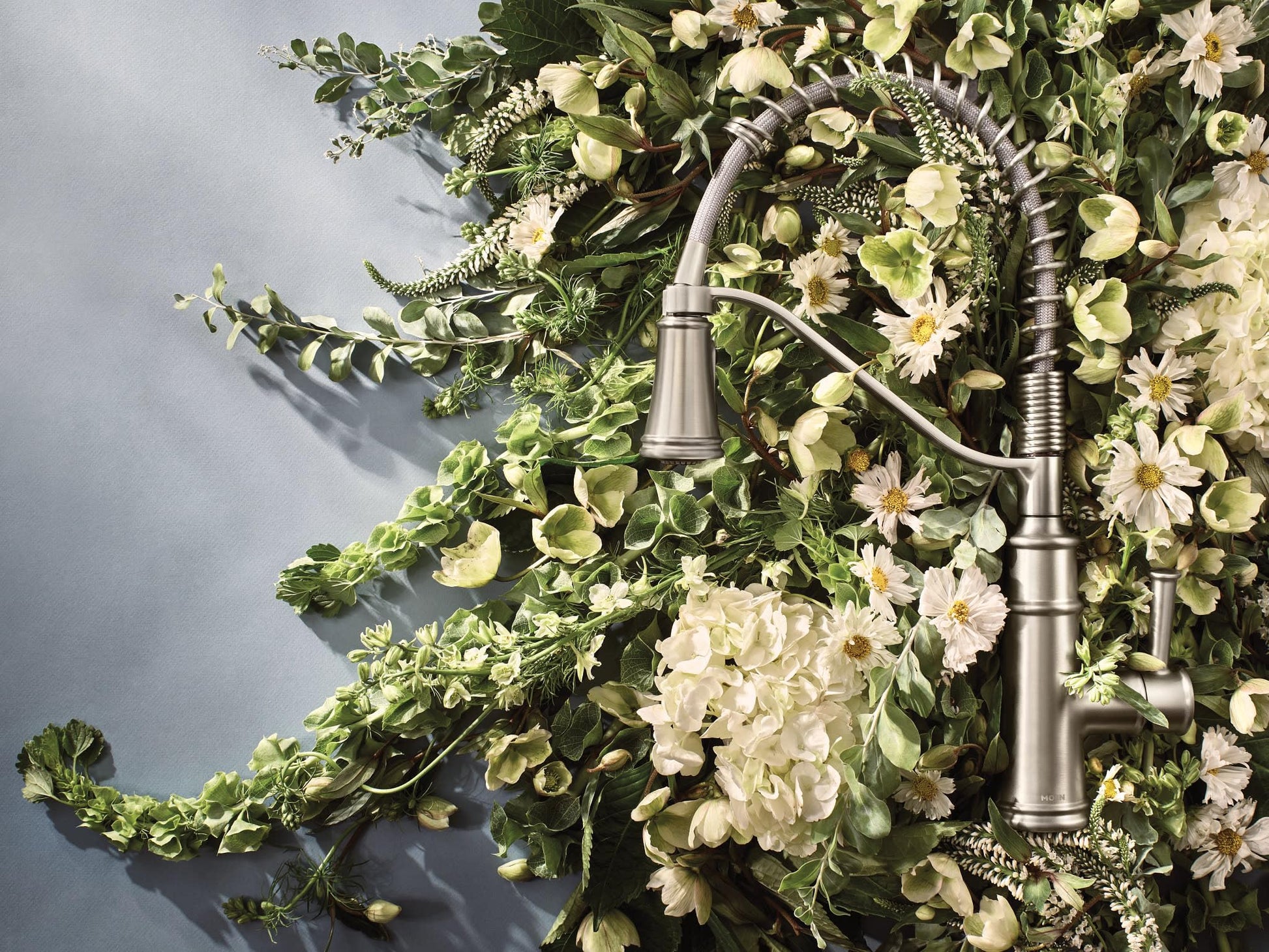 Stainless steel kitchen faucet with single handle and pull-down sprayer against floral backdrop.