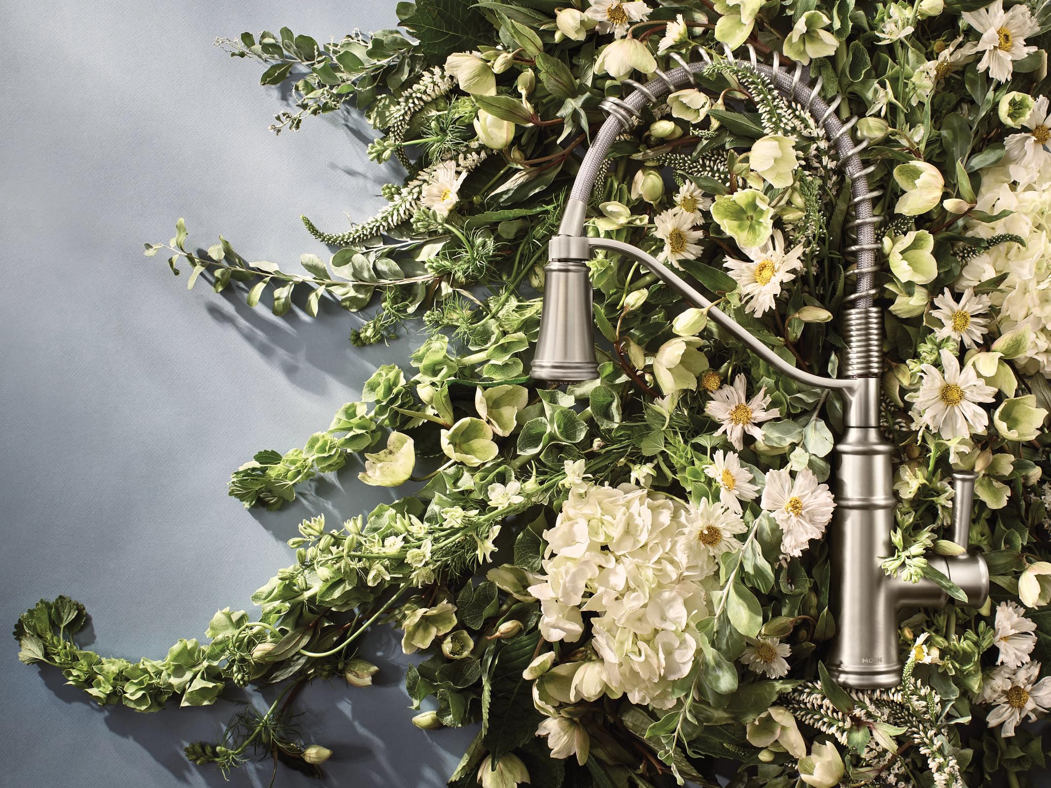 Stainless steel kitchen faucet with single handle and pull-down sprayer against floral backdrop.
