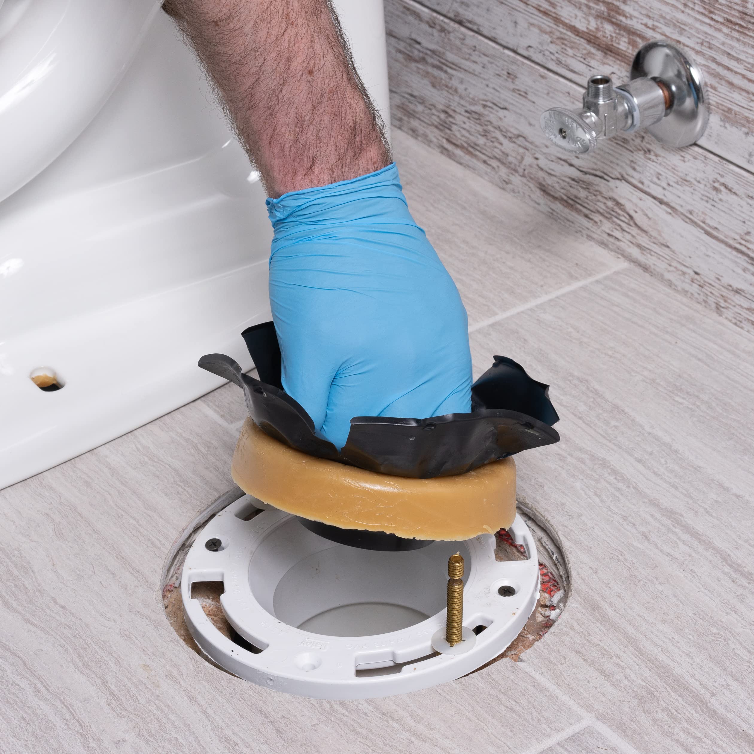 Hand in blue glove positioning tan wax ring with black flange onto white toilet base flange during installation.