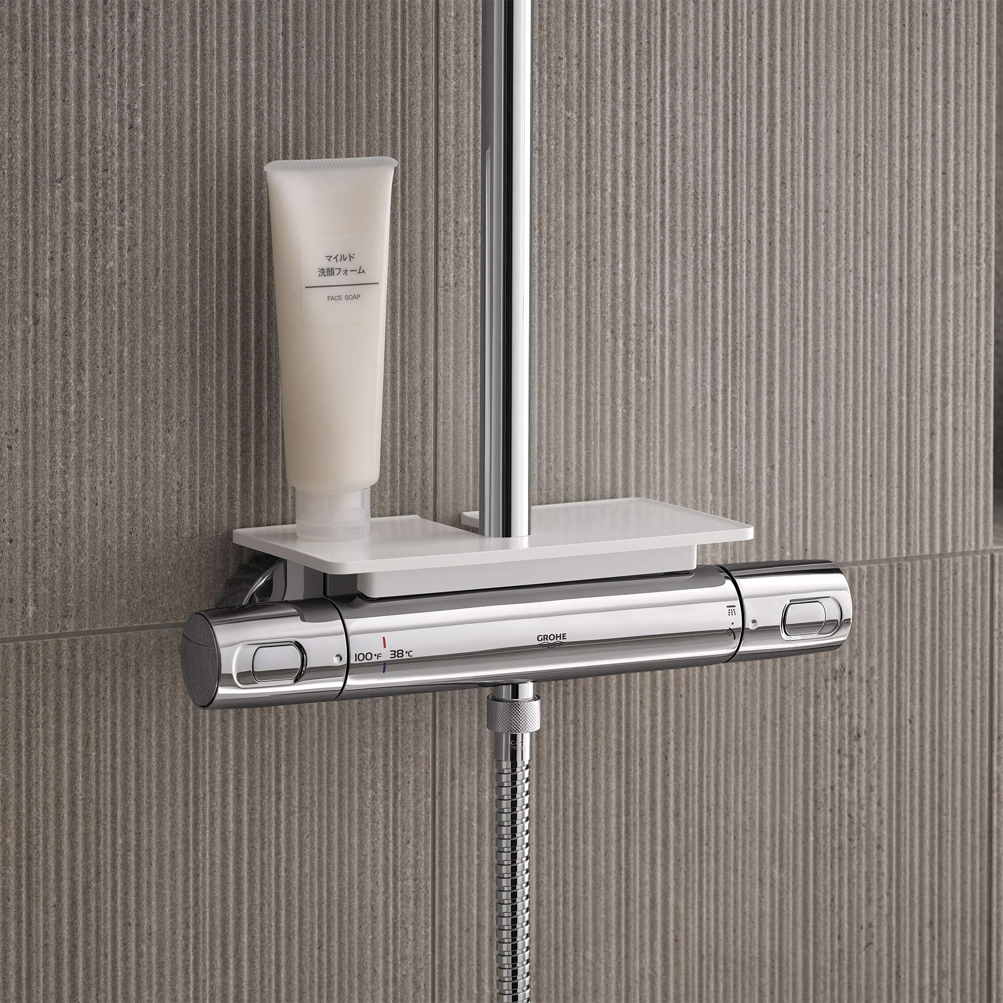 Chrome thermostatic shower system with horizontal bar control, white shelf, and hose attachment on tiled bathroom wall.