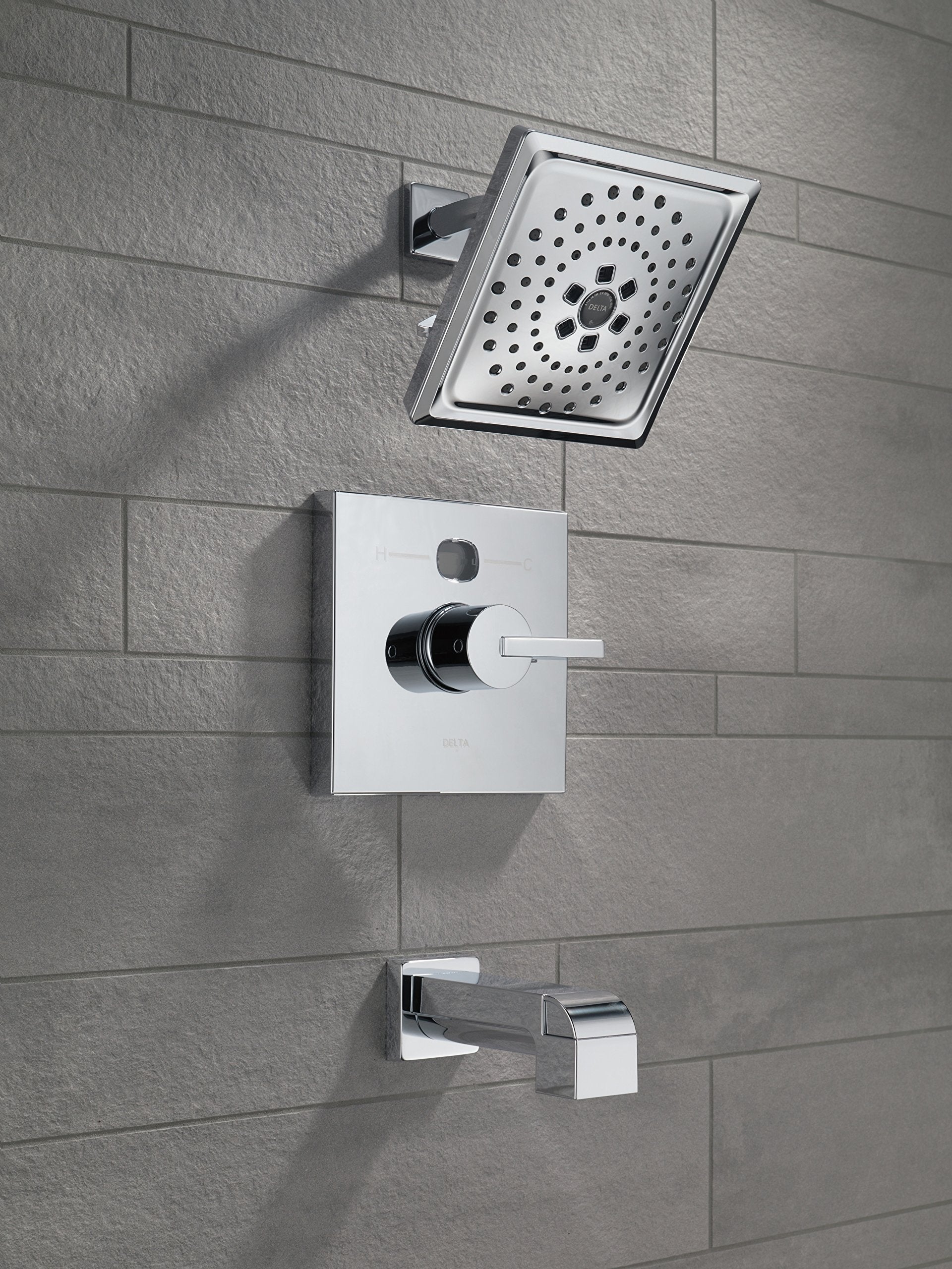 Chrome shower system mounted on gray tile wall with square showerhead, control valve, and tub spout.