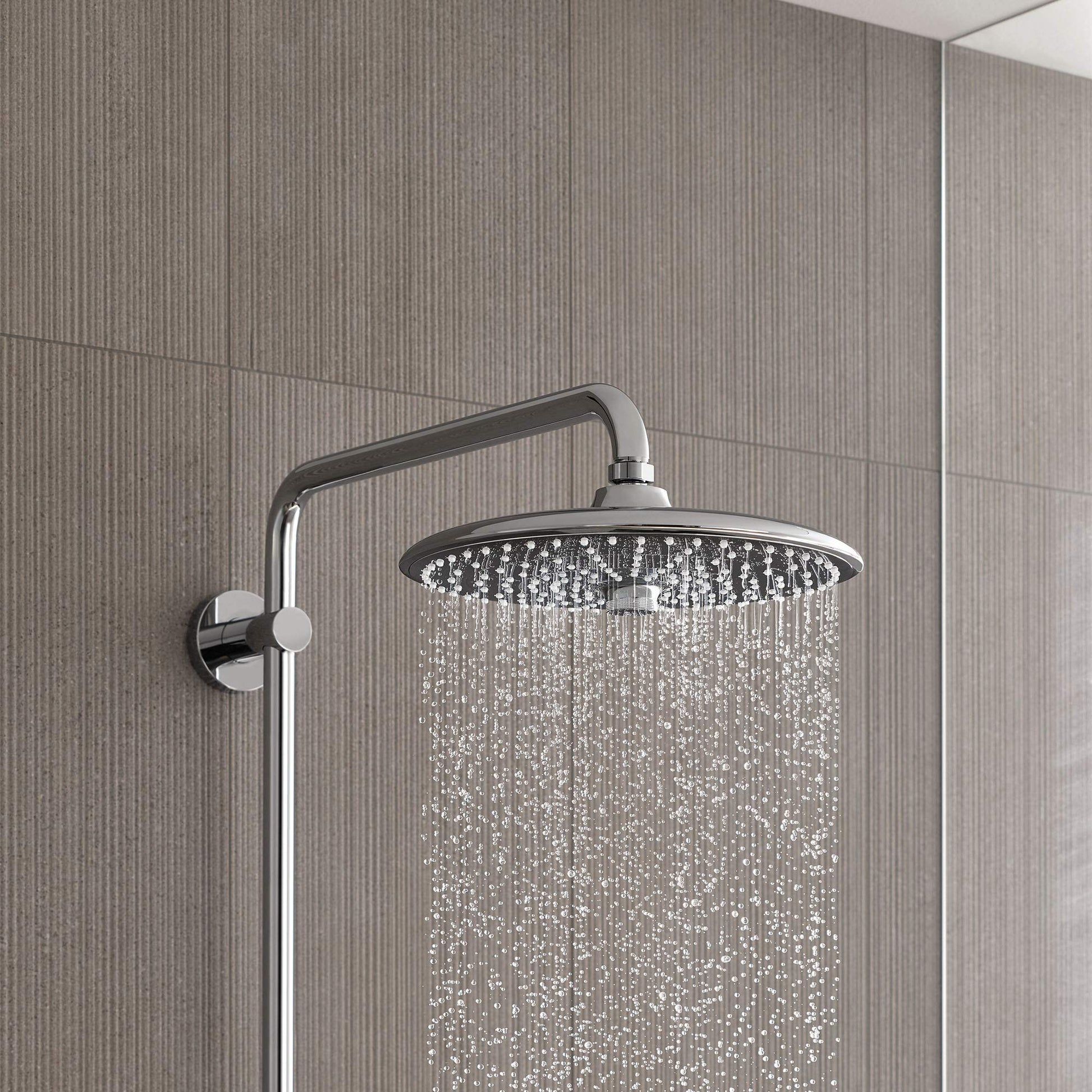 Chrome showerhead with 10-inch round face mounted on curved arm against textured tile wall.