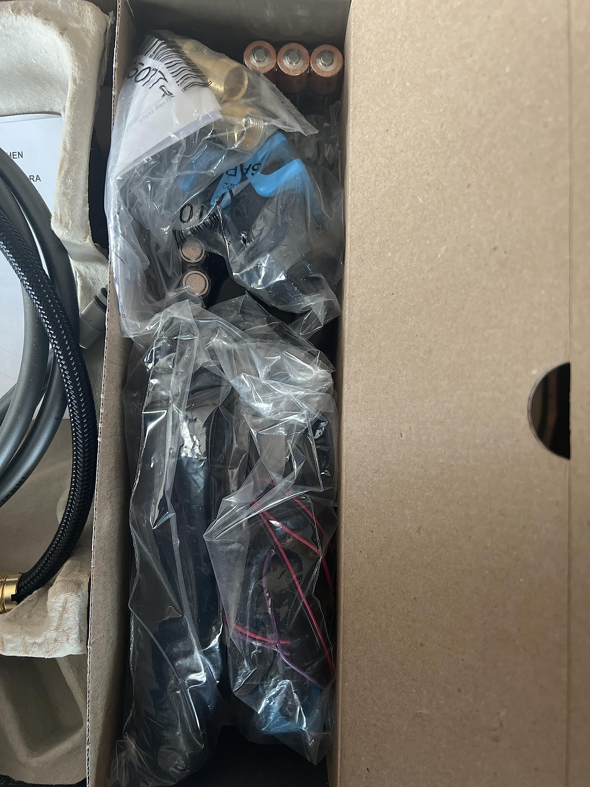 Kitchen faucet components in cardboard box including spout, hardware, and wiring wrapped in plastic.