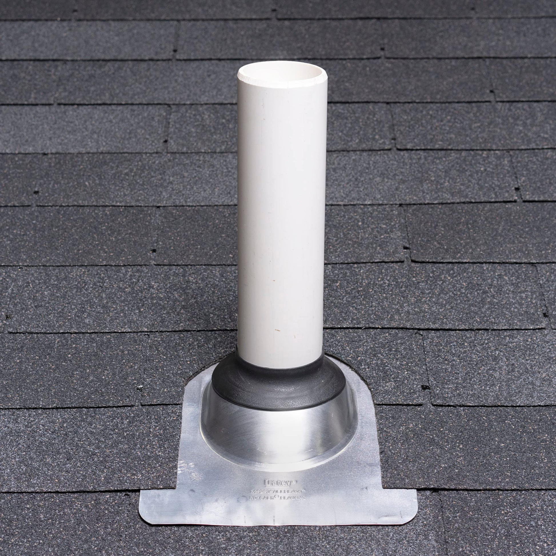 Silver aluminum roof flashing with white cylindrical vent pipe and black rubber collar, mounted on asphalt shingle roof.
