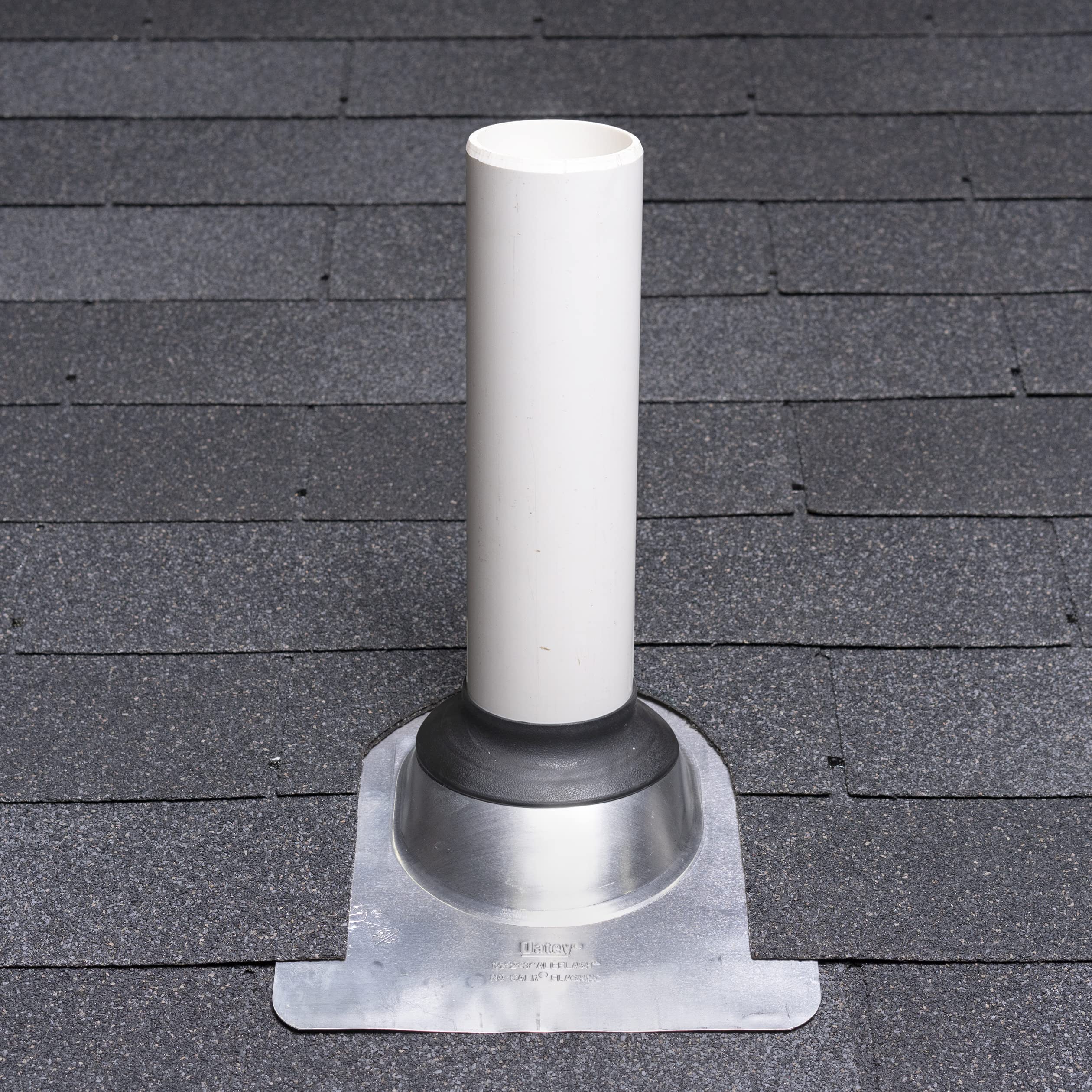 Silver aluminum roof flashing with white cylindrical vent pipe and black rubber collar, mounted on asphalt shingle roof.
