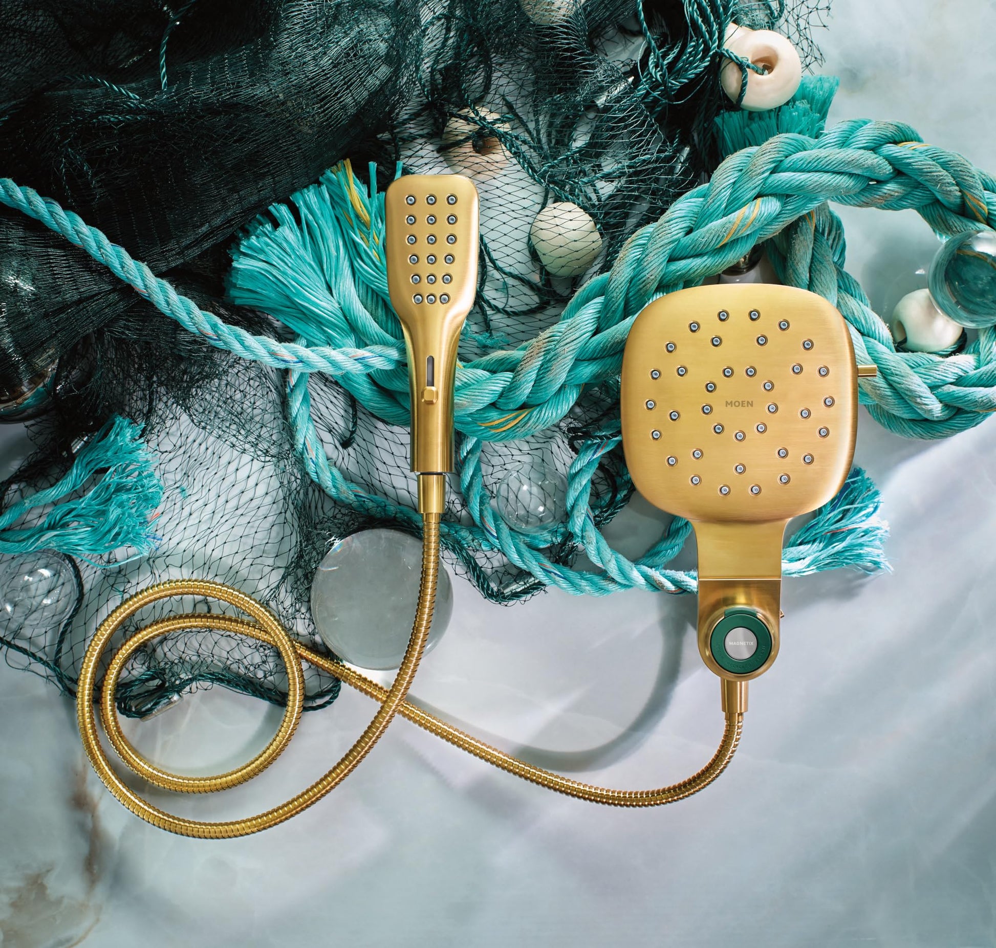 Brushed gold square rainfall shower head and detachable handheld shower with hose displayed on nautical rope background.