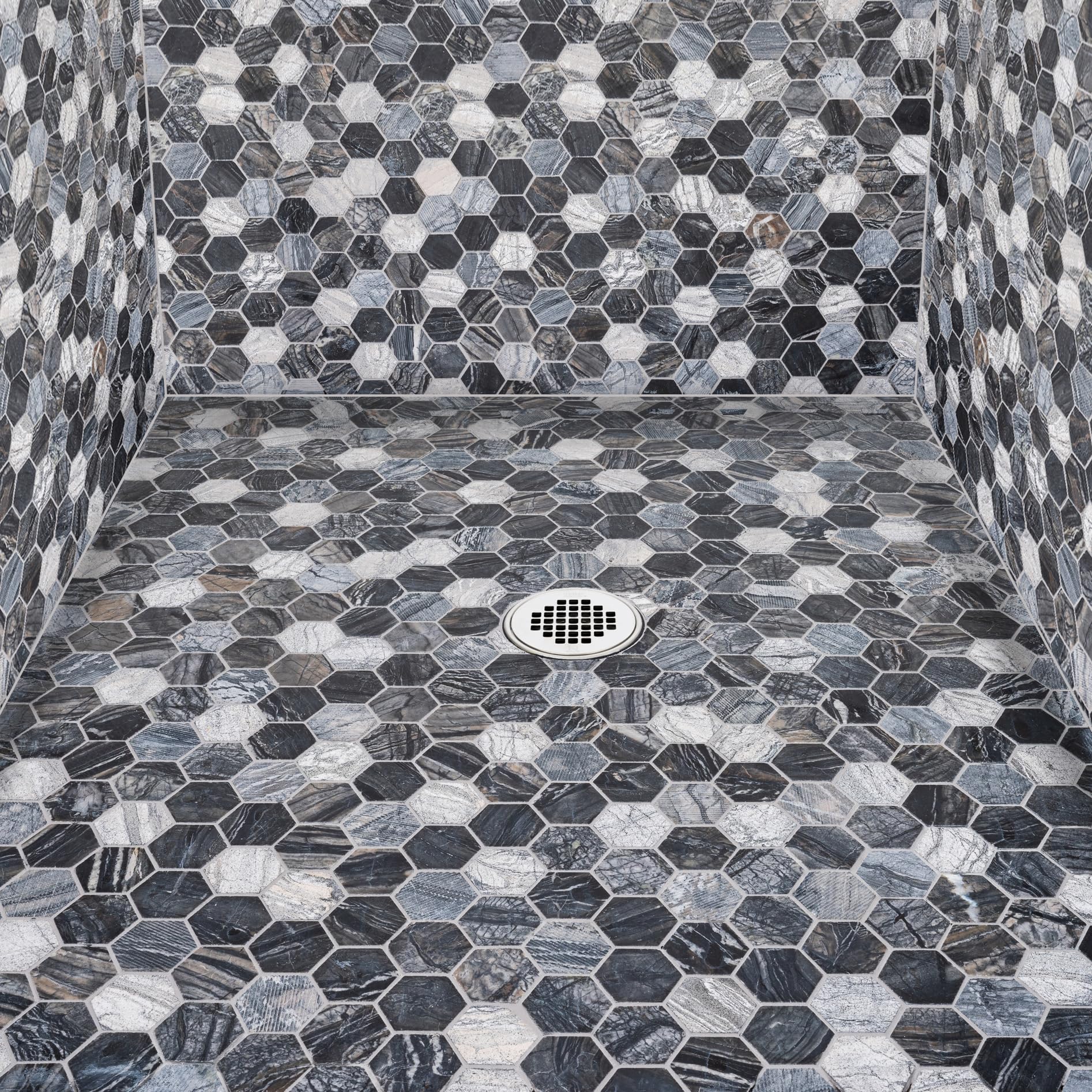 Satin nickel shower strainer with square perforated grate mounted on hexagonal tile shower floor.