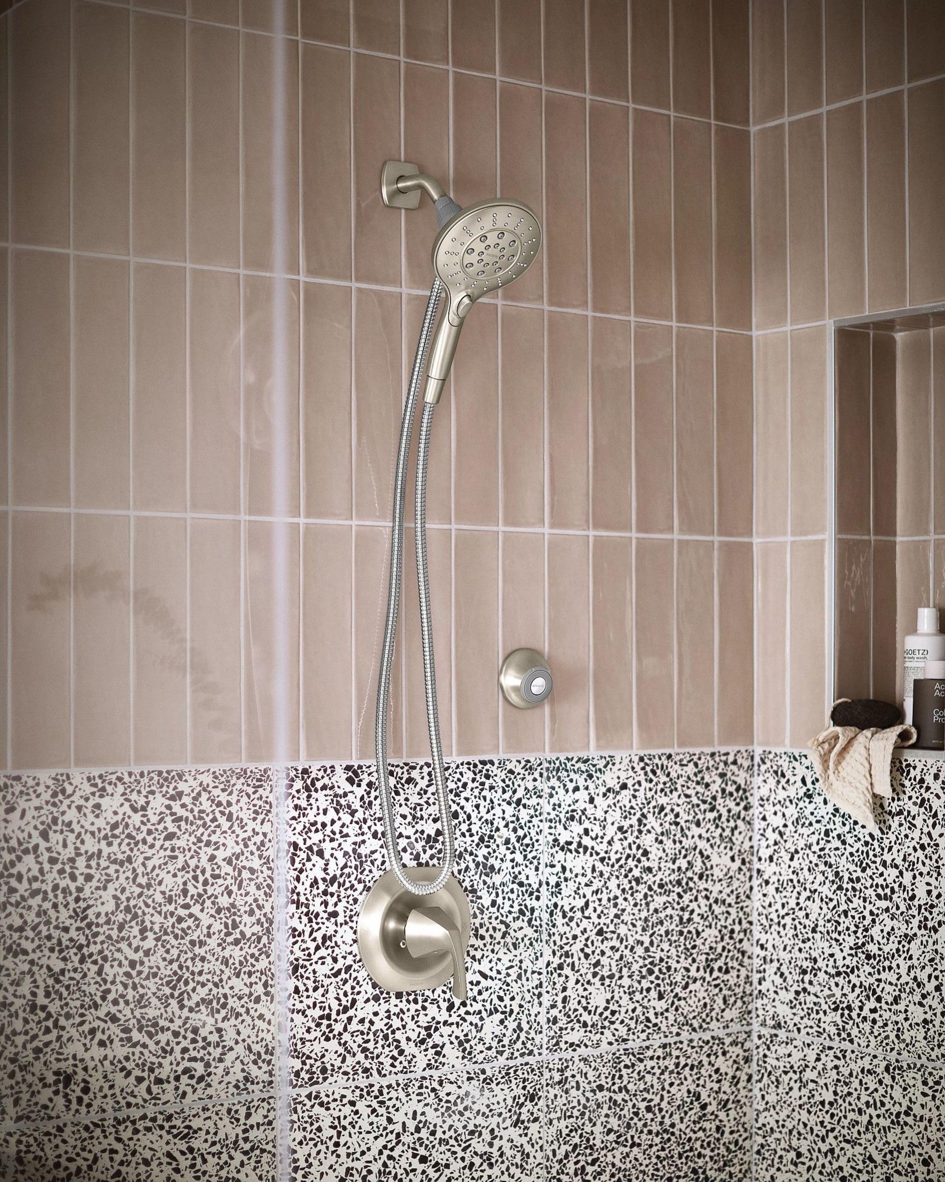 Brushed nickel showerhead with handheld wand and magnetic cradle mounted on shower wall with beige and speckled tile.