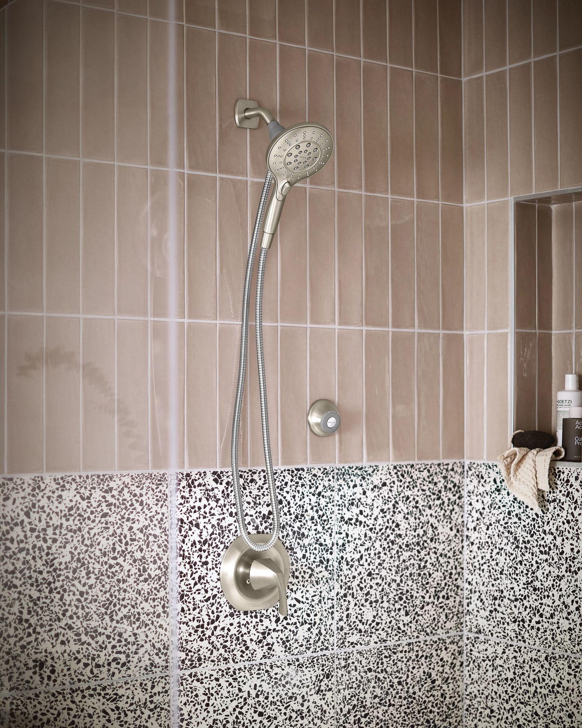 Brushed nickel showerhead with handheld wand and magnetic cradle mounted on shower wall with beige and speckled tile.