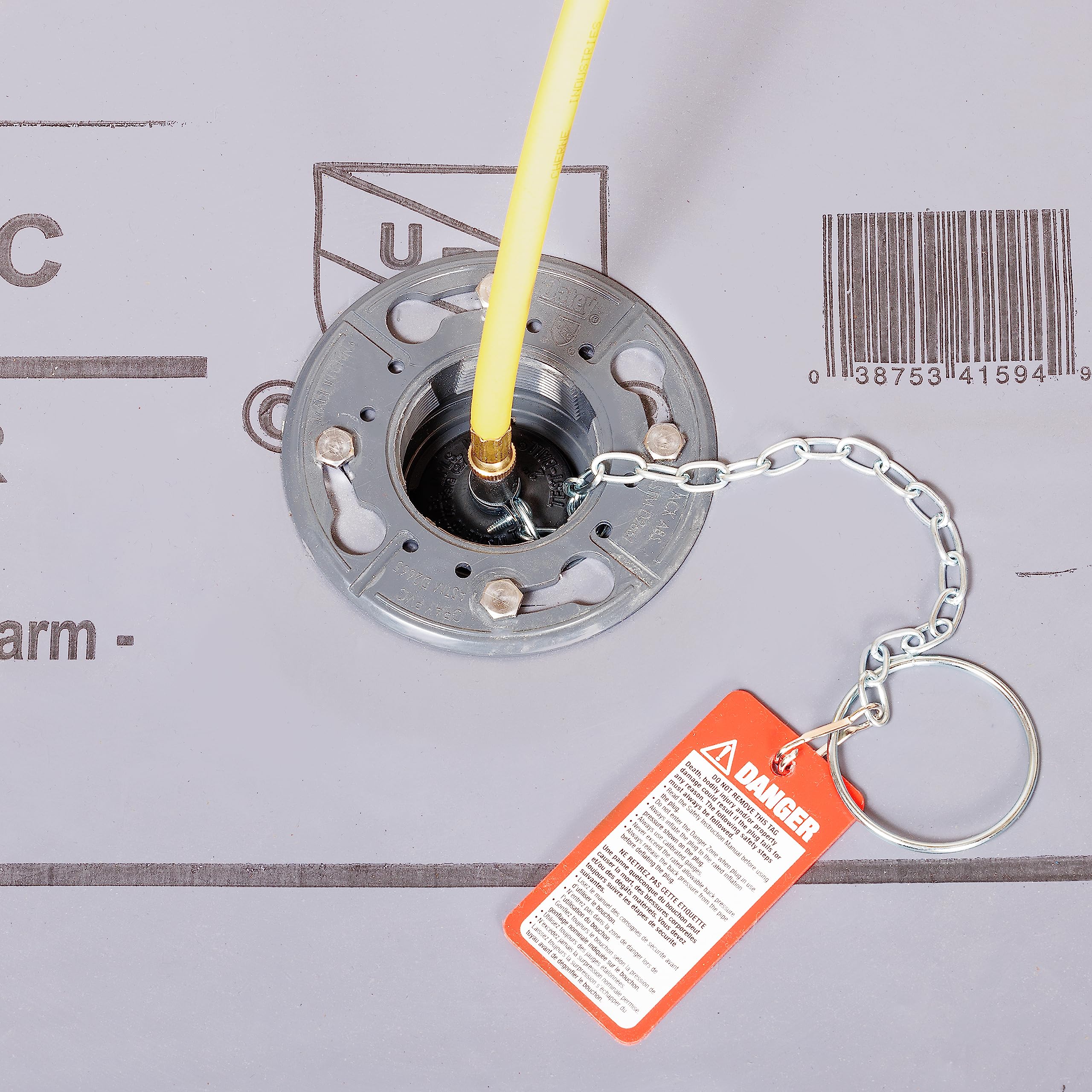 Black inflatable test-ball plug with yellow inflation tube, metal flange base, and orange warning tag with chain attachment.
