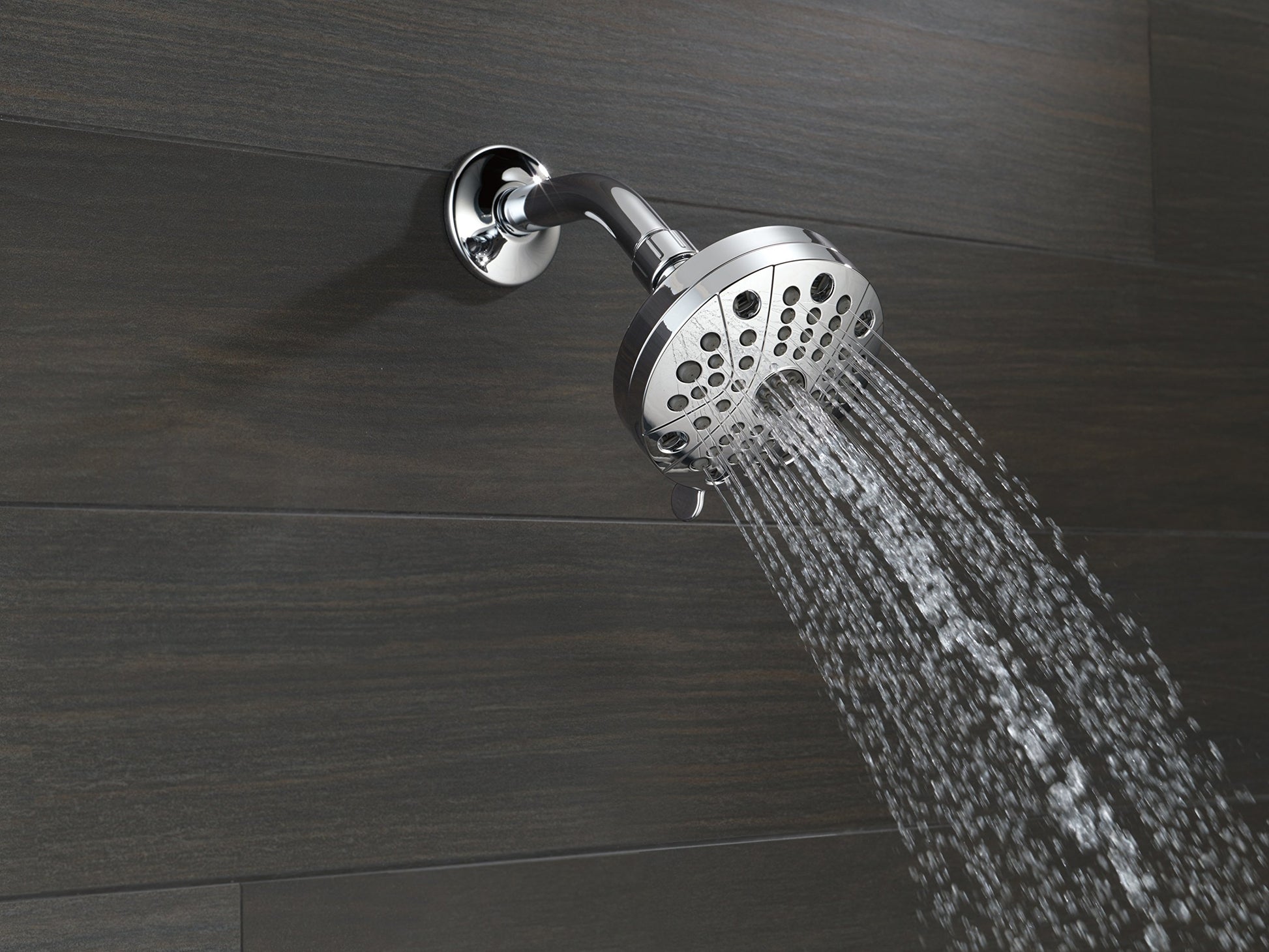 Chrome shower head with circular flange mounted on wall, water streaming downward.