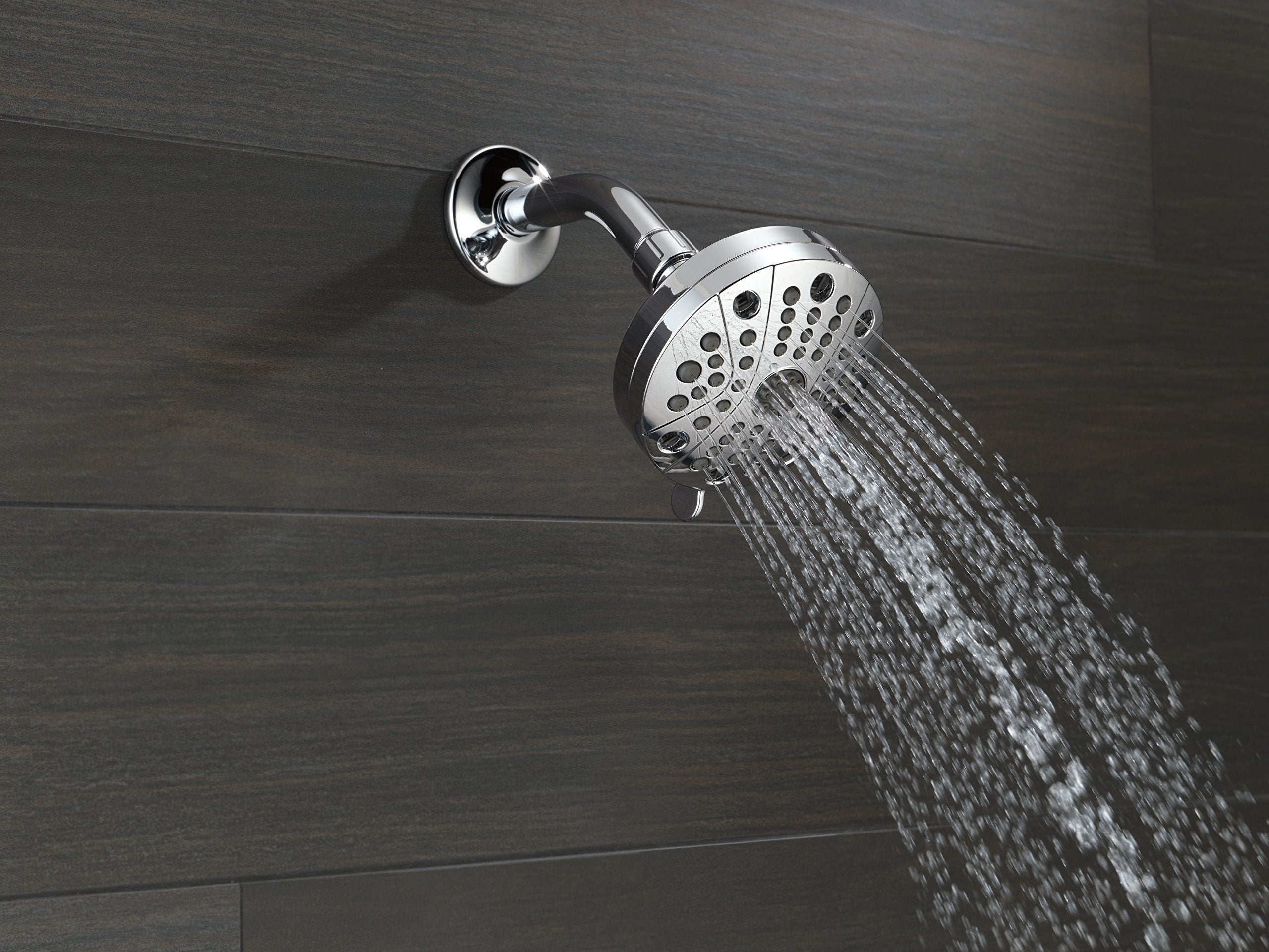 Chrome shower head with circular flange mounted on wall, water streaming downward.