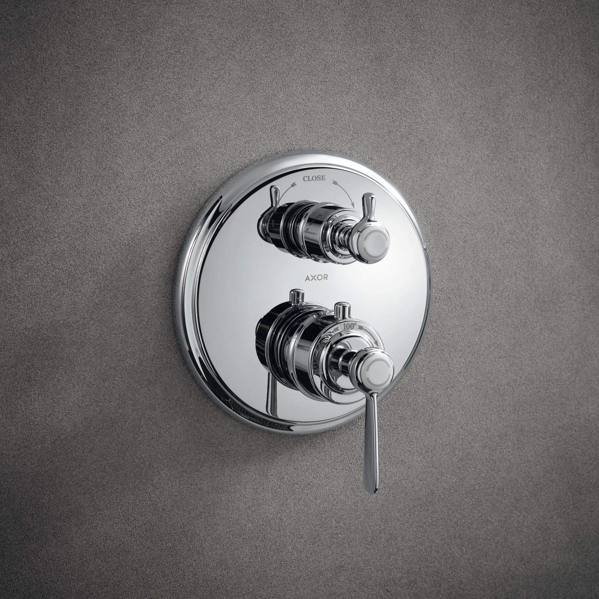 Polished nickel thermostatic shower trim with dual handles, diverter valve, and circular trim ring mounted on gray wall.