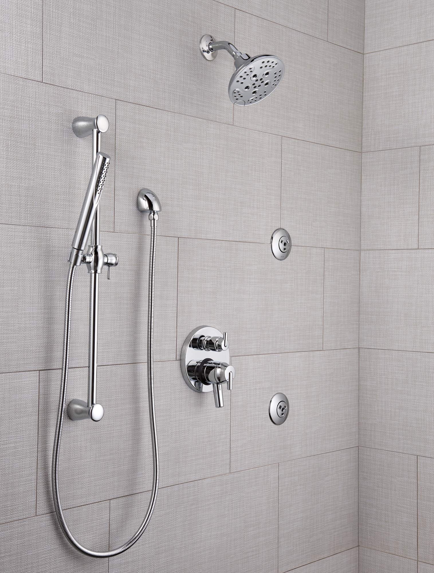 Chrome shower system with overhead rainfall showerhead, handheld spray wand, control valve, and body jets mounted on tile wal