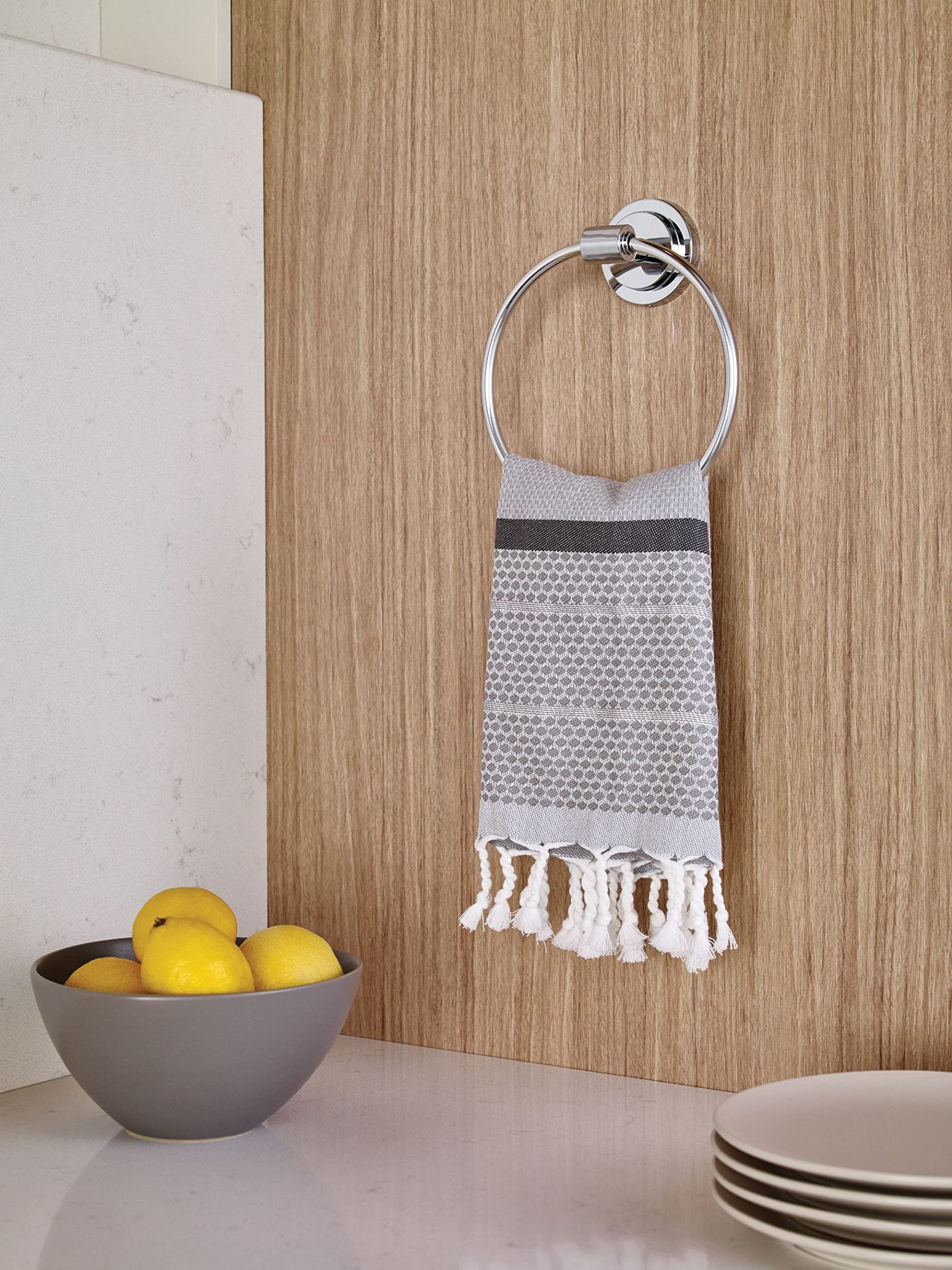 Chrome wall-mounted towel ring with circular design holding a gray and white patterned hand towel.